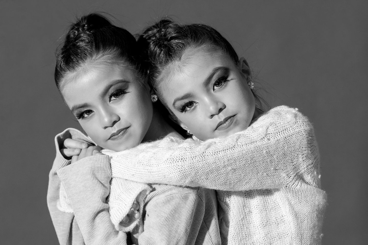 Black and white portrait of two identical twins wearing white sweaters posing close together.