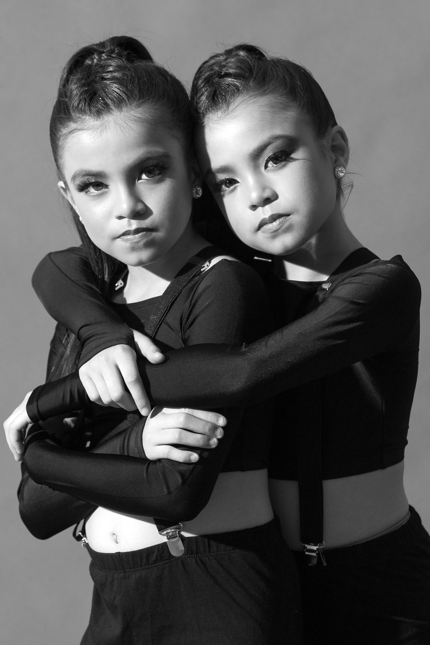 Black and white photo series showing two children embracing in matching black outfits against neutral background.