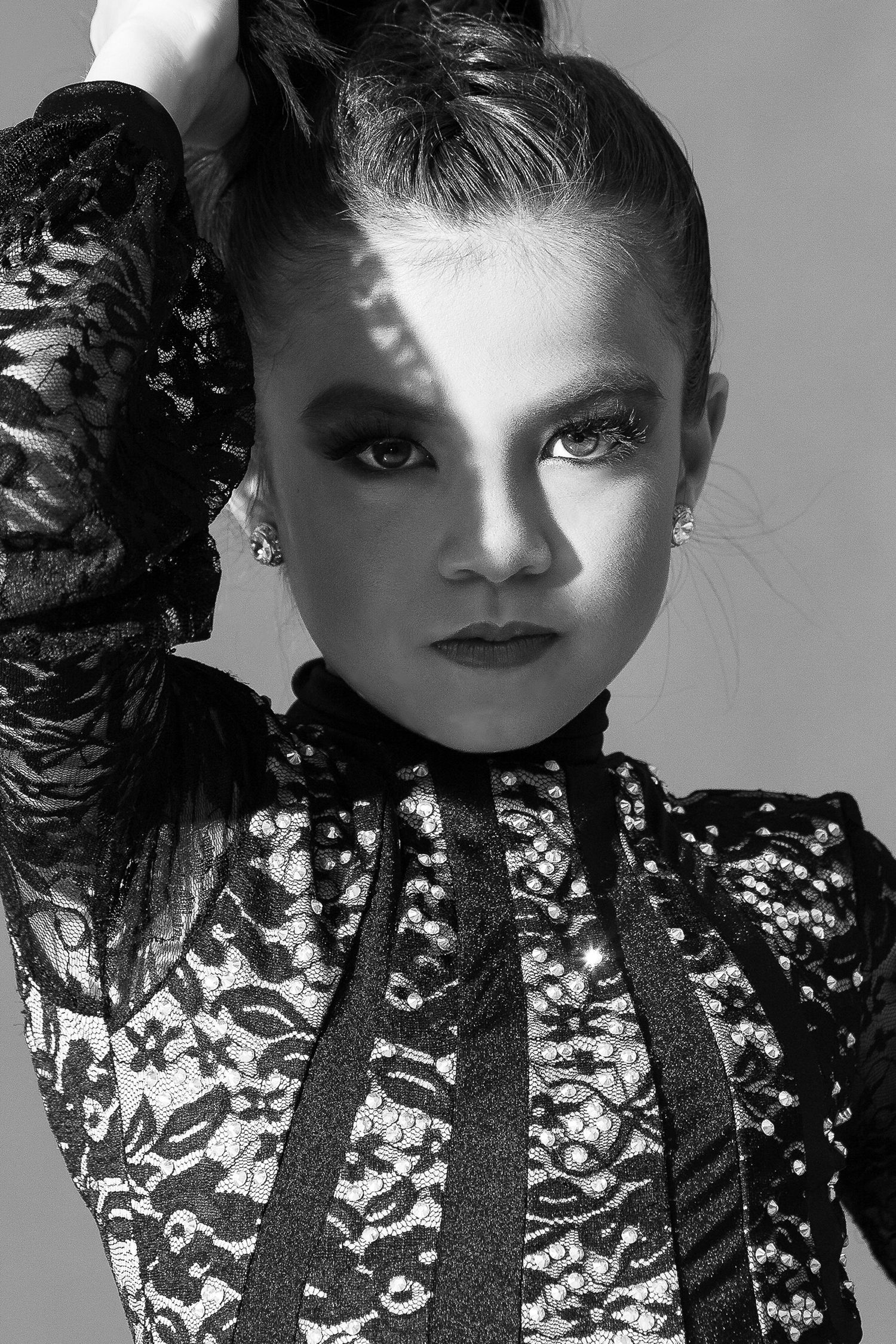 Black and white close-up fashion portrait featuring dramatic makeup and a lace high-neck top.