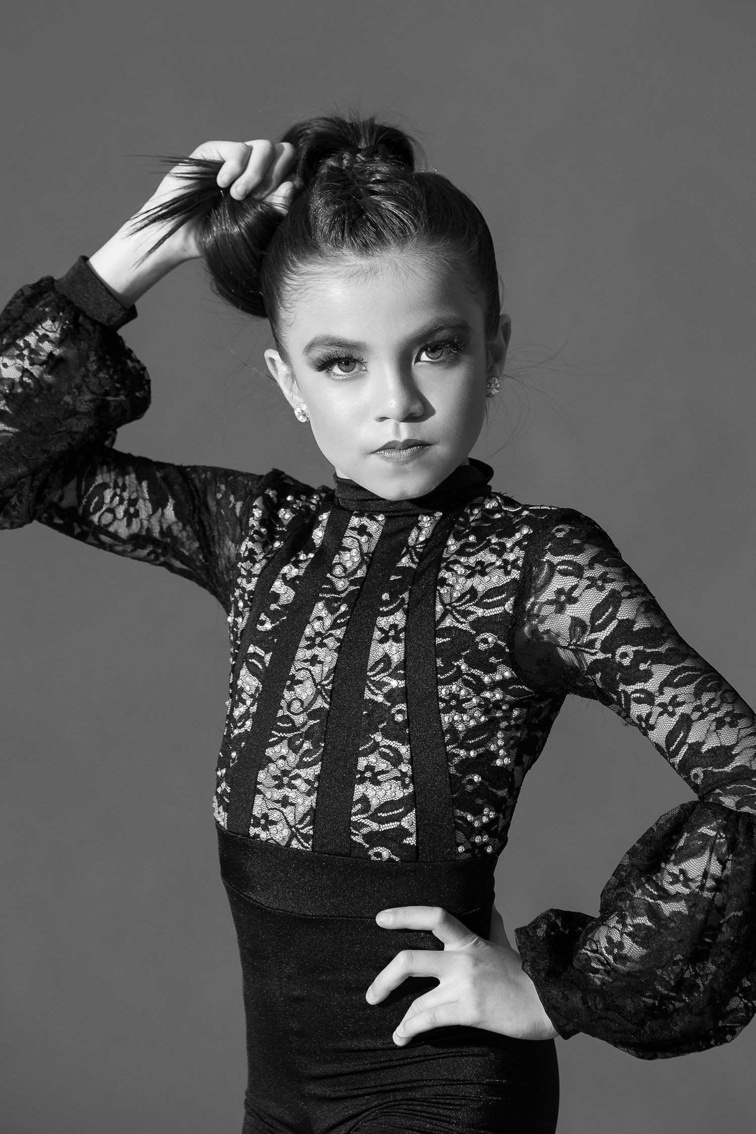 Black and white portrait of a young model wearing a long sleeve lace dress with dramatic styling.