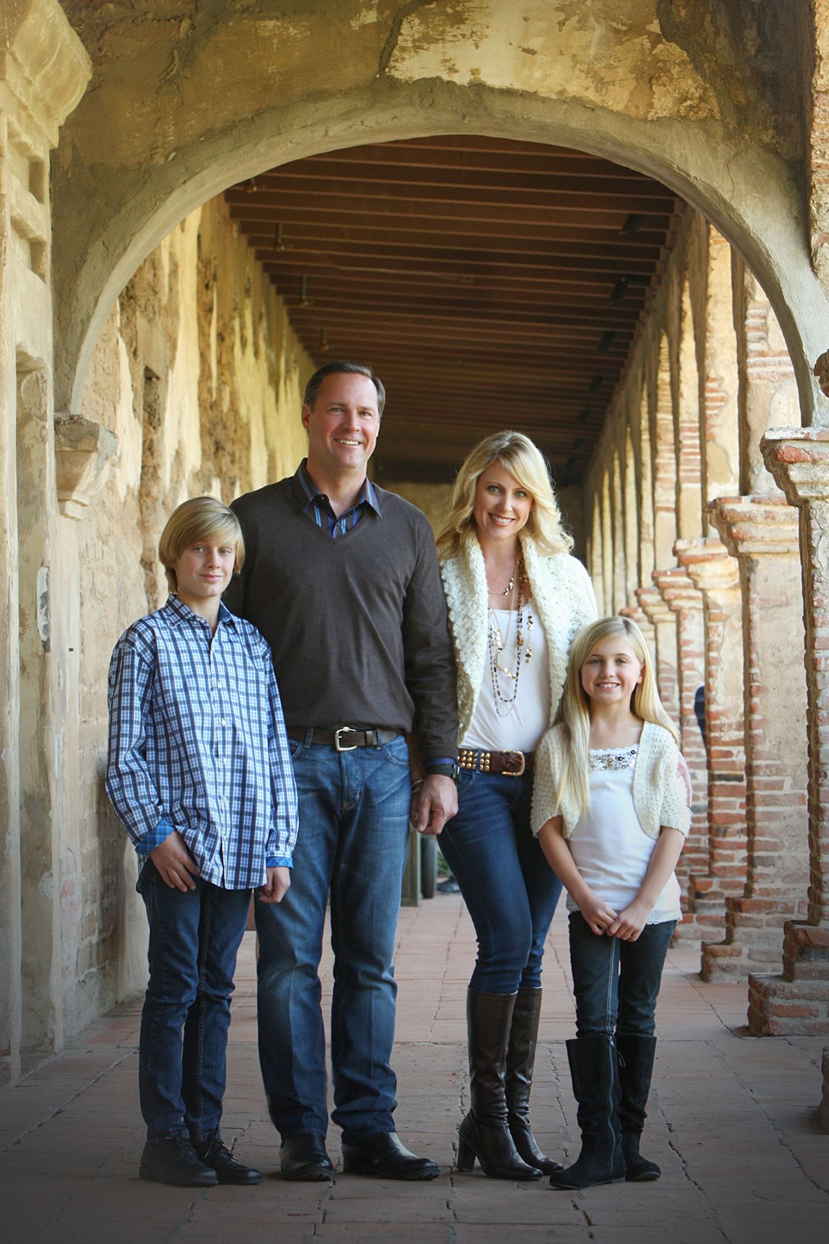 Family of four posed under historic mission archway in casual attire.