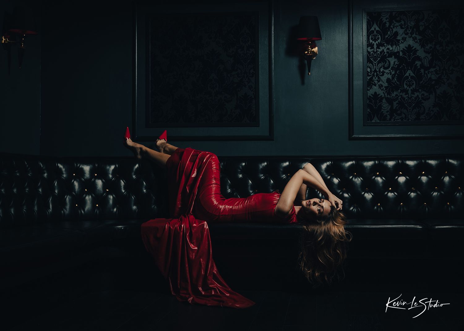 Dramatic photo of figure in red dress reclining on dark leather couch.