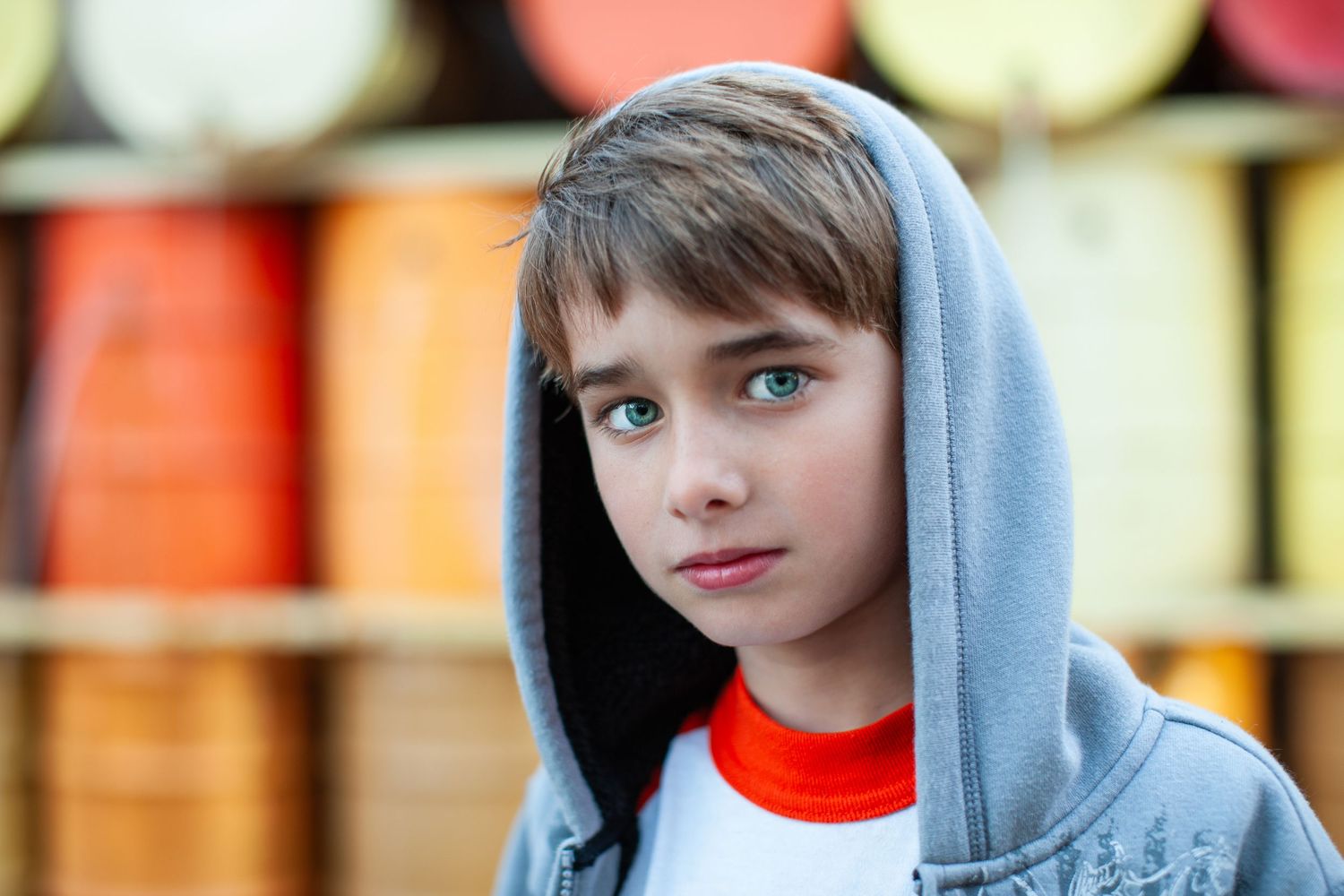 A youth in a light gray hoodie stands against a colorful blurred background of orange and yellow tones.