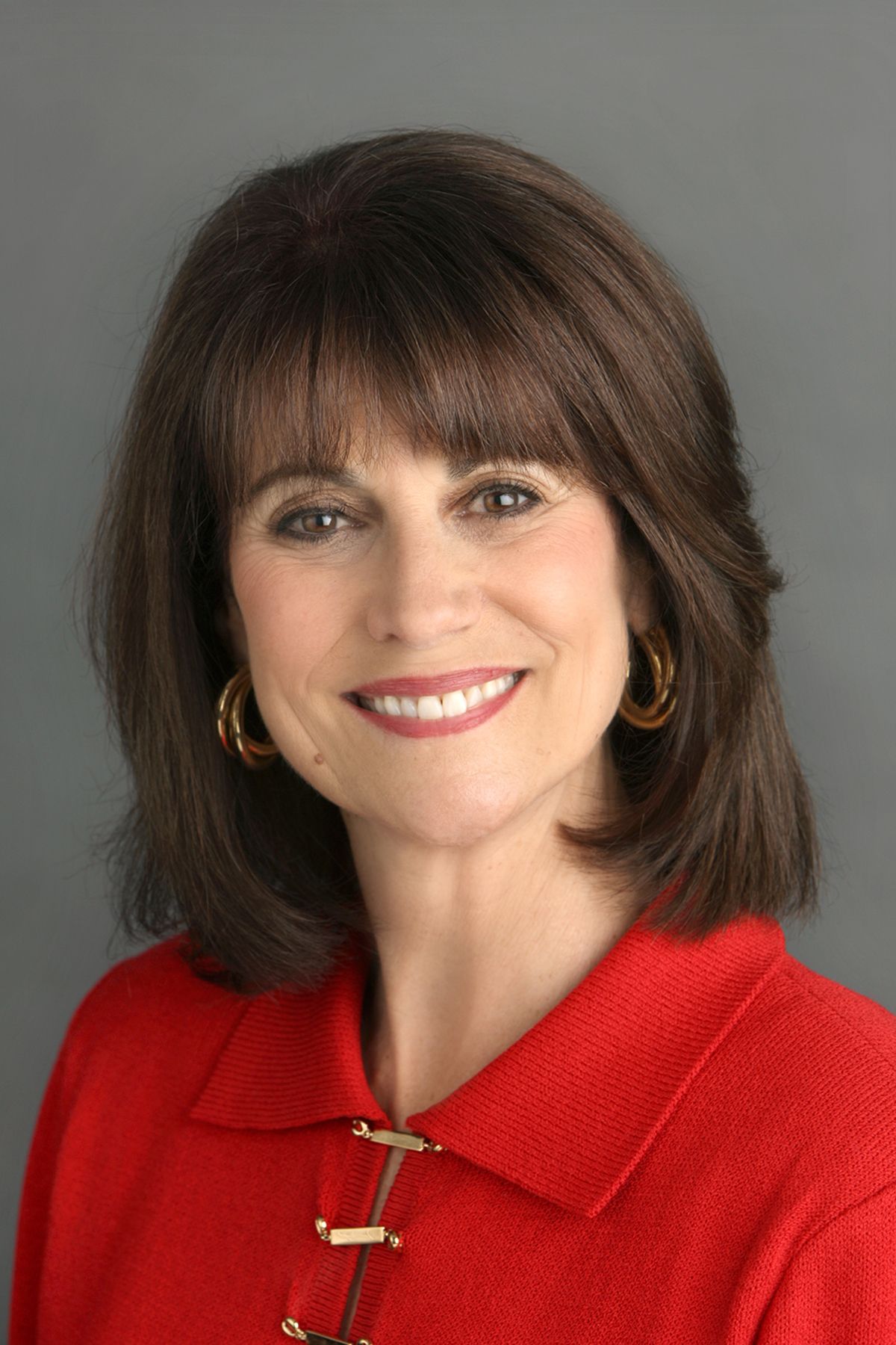 Professional portrait of woman in red blazer against grey background.