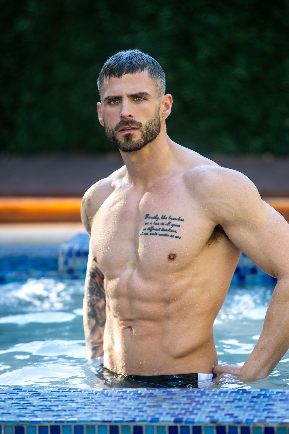 Athletic person lounging in a swimming pool edge showing muscular physique and tattoos.