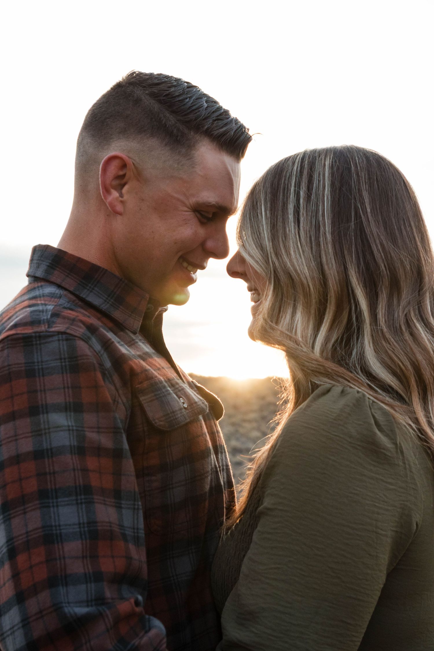 Couple sharing a romantic sunset moment, smiling and touching foreheads on a beach.