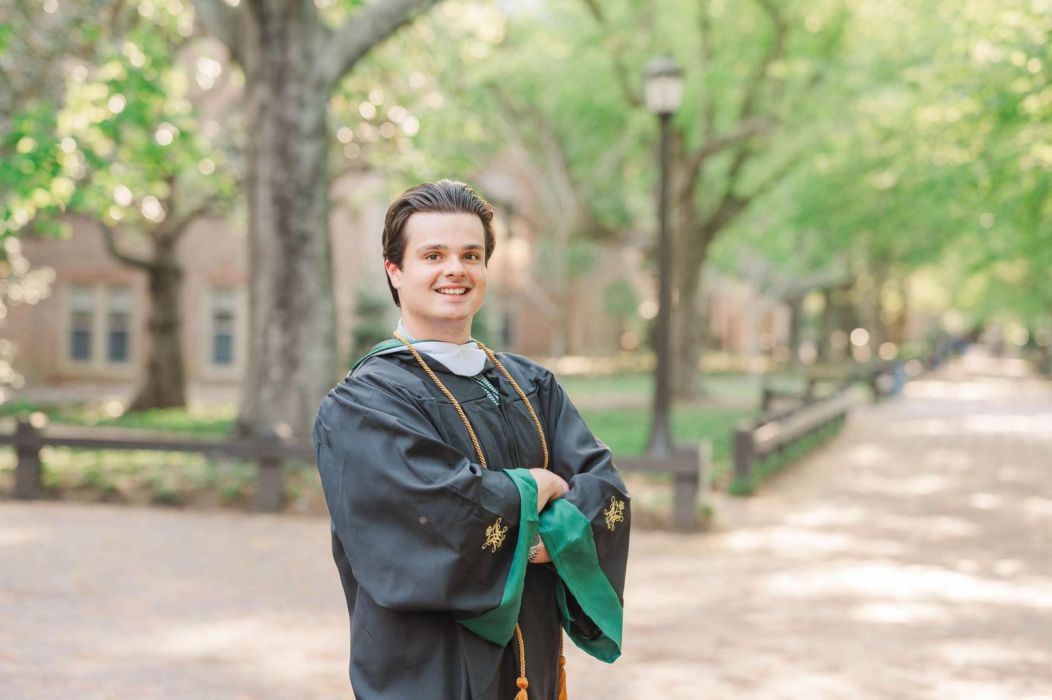 A graduate in dark cap and gown poses outdoors on campus during graduation season. William and Mary