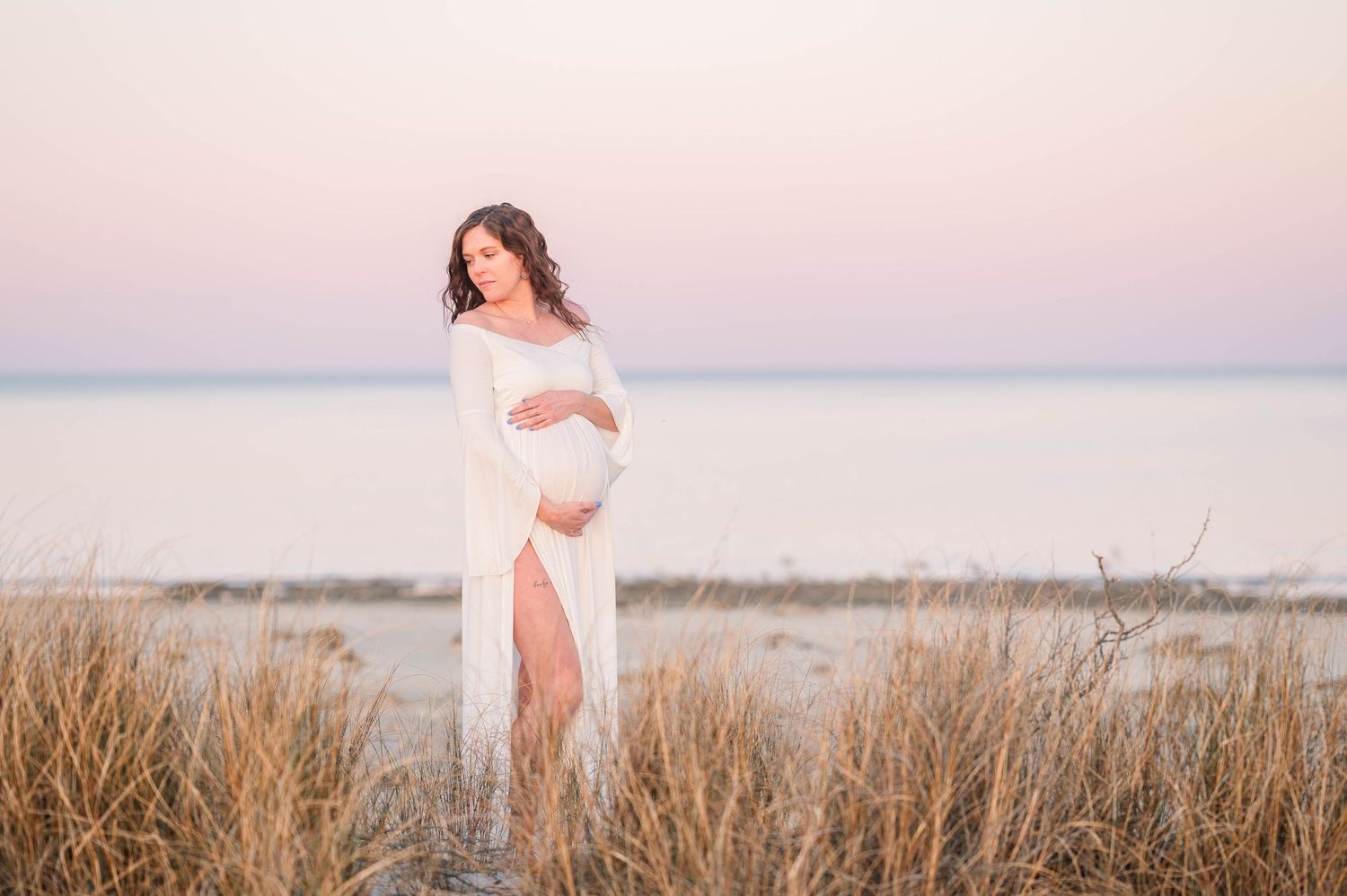 Maternity photo session in flowing white dress at sunset in field.