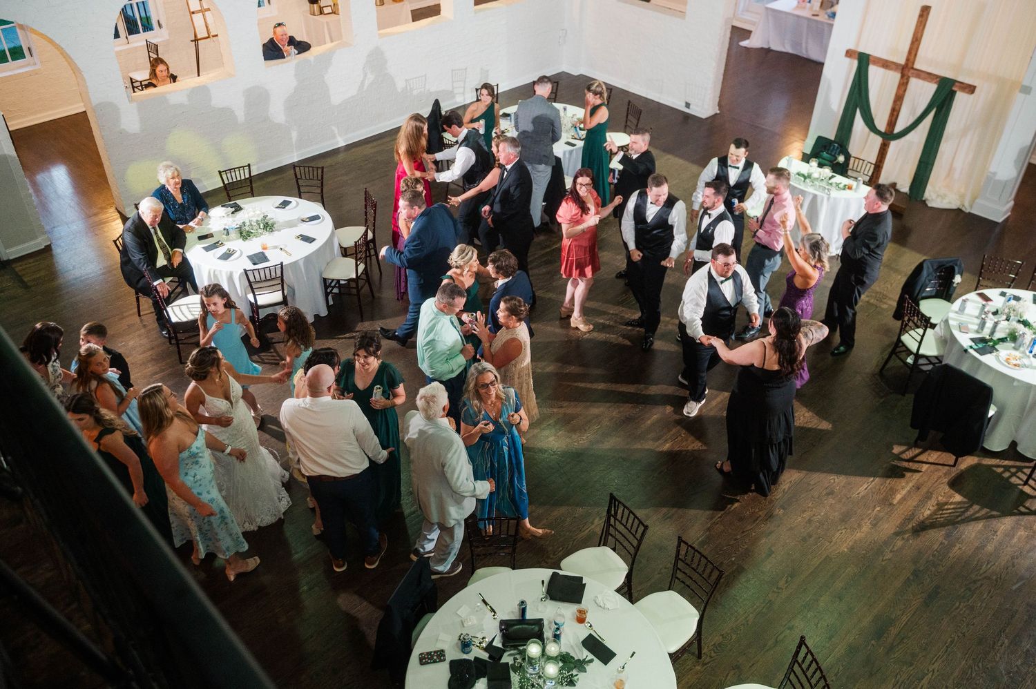 Large group of wedding guests gathered at an indoor reception with round tables.