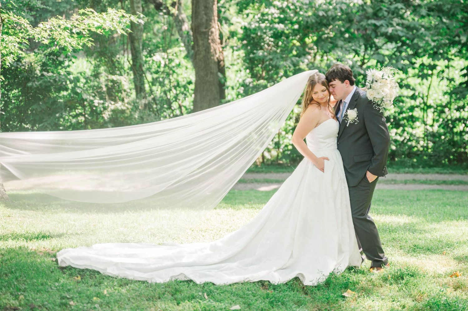 Elegant wedding veil flows dramatically in outdoor garden setting.