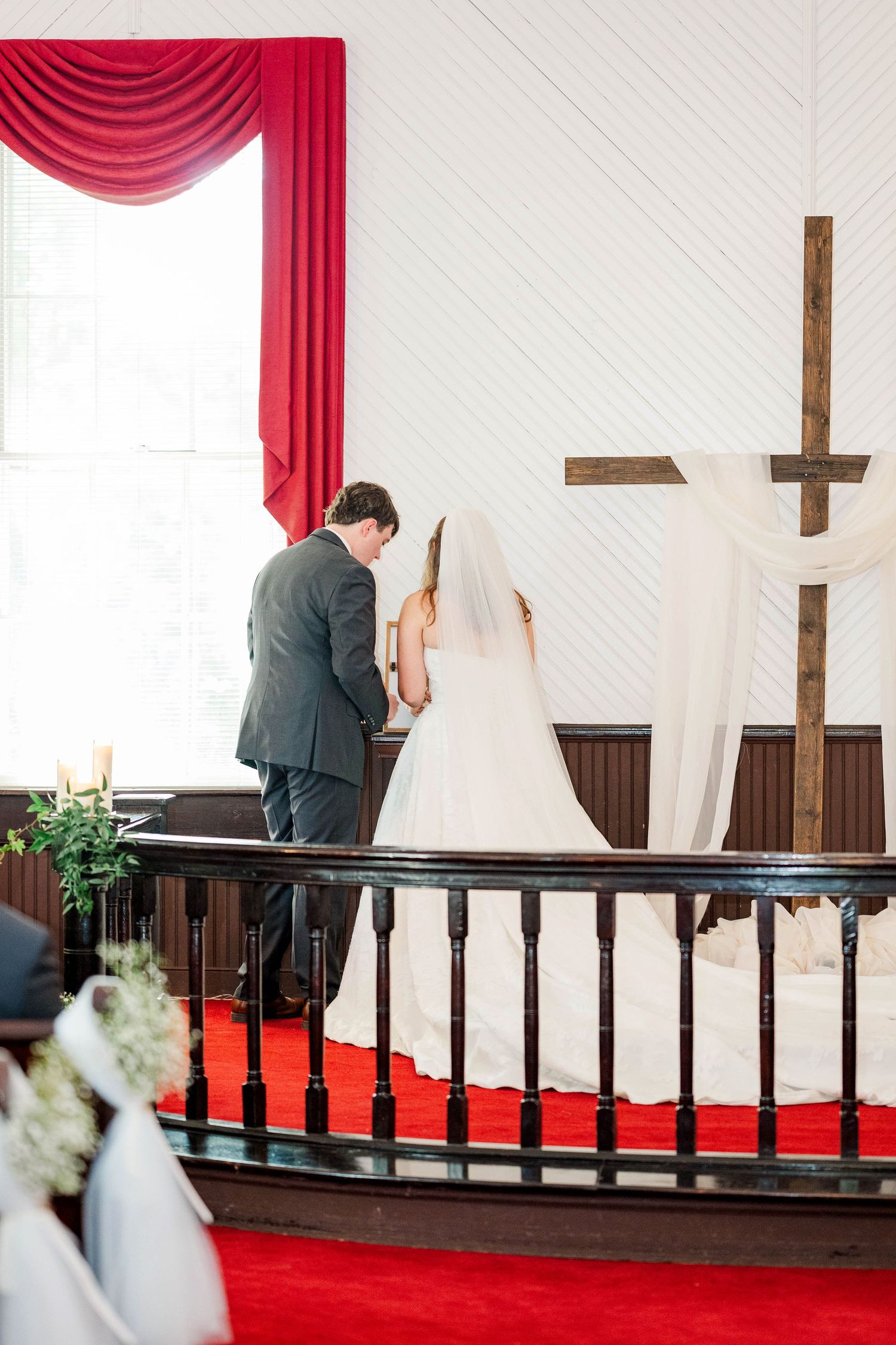 Traditional church wedding ceremony with red drapes and wooden cross in the background.