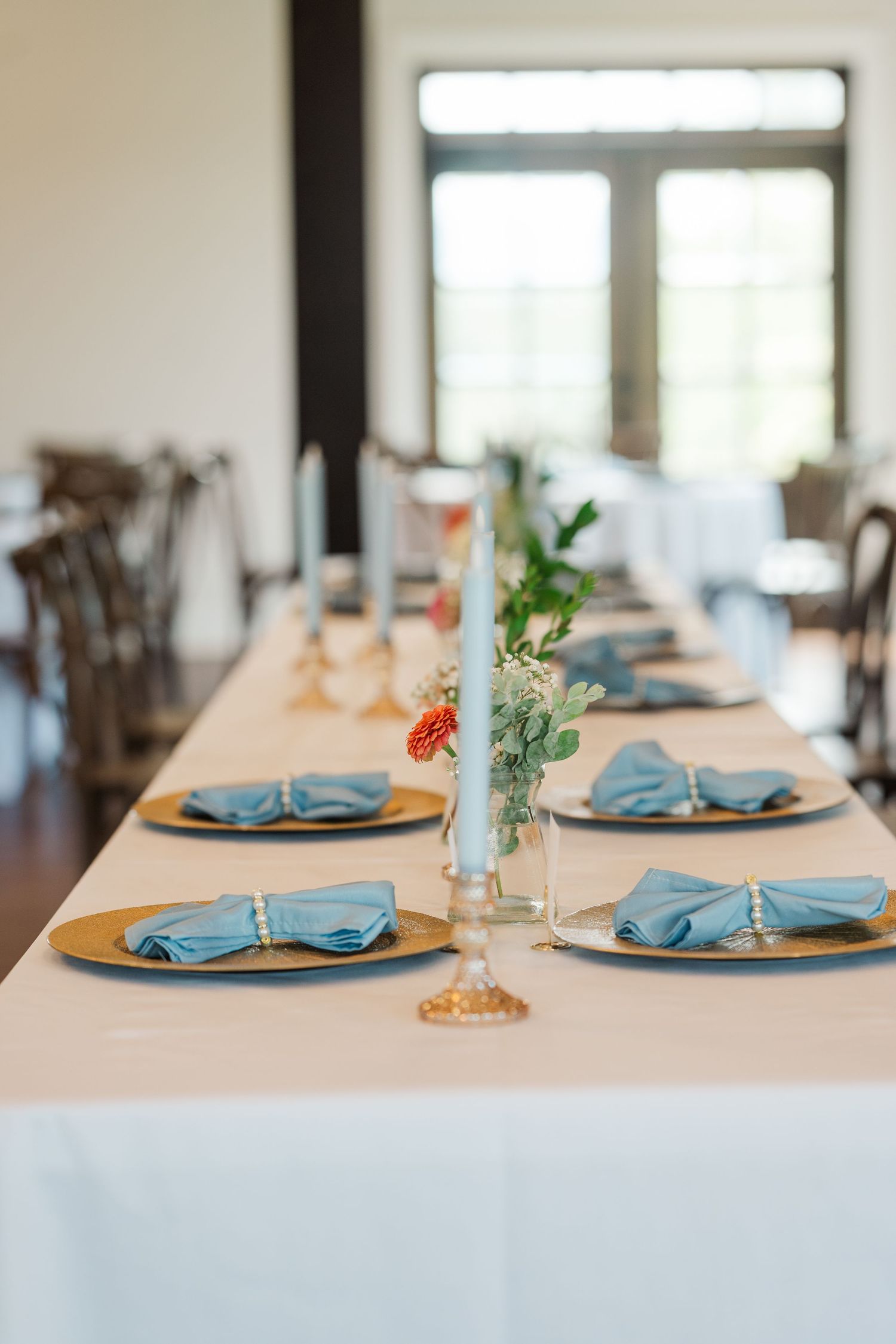 Wedding reception table set with blue napkins on gold chargers and floral centerpieces.