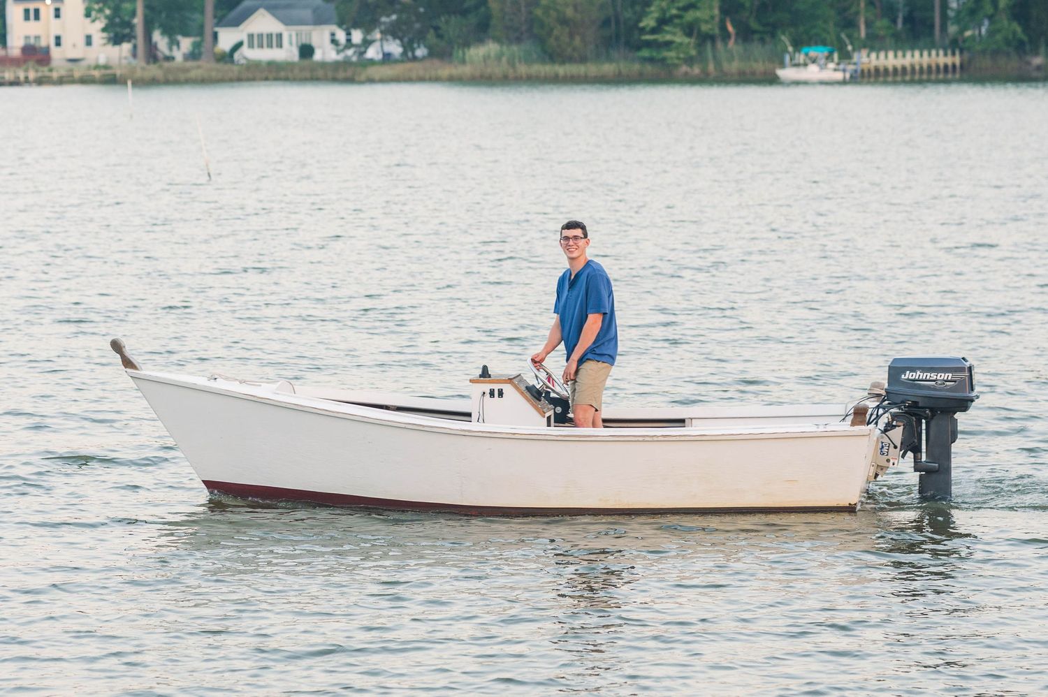 Small white boat with outboard motor glides across calm waters near coastal homes.