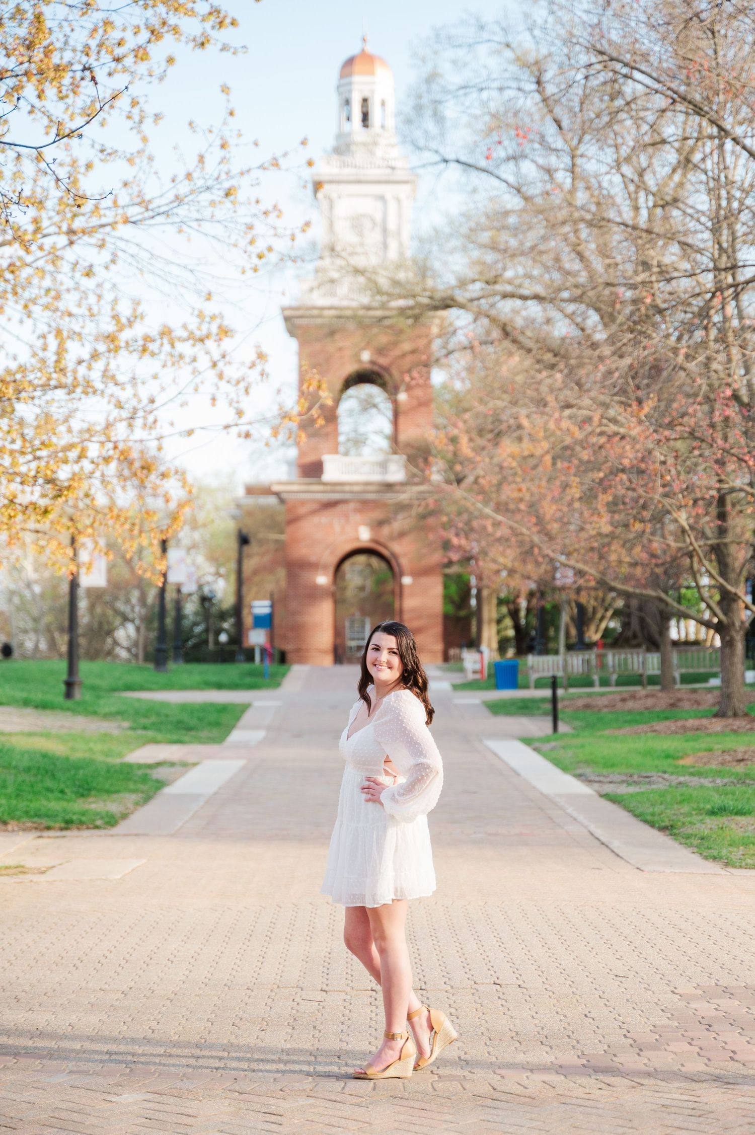White brick pathway leading to a church bell tower surrounded by autumn trees on a college campus.