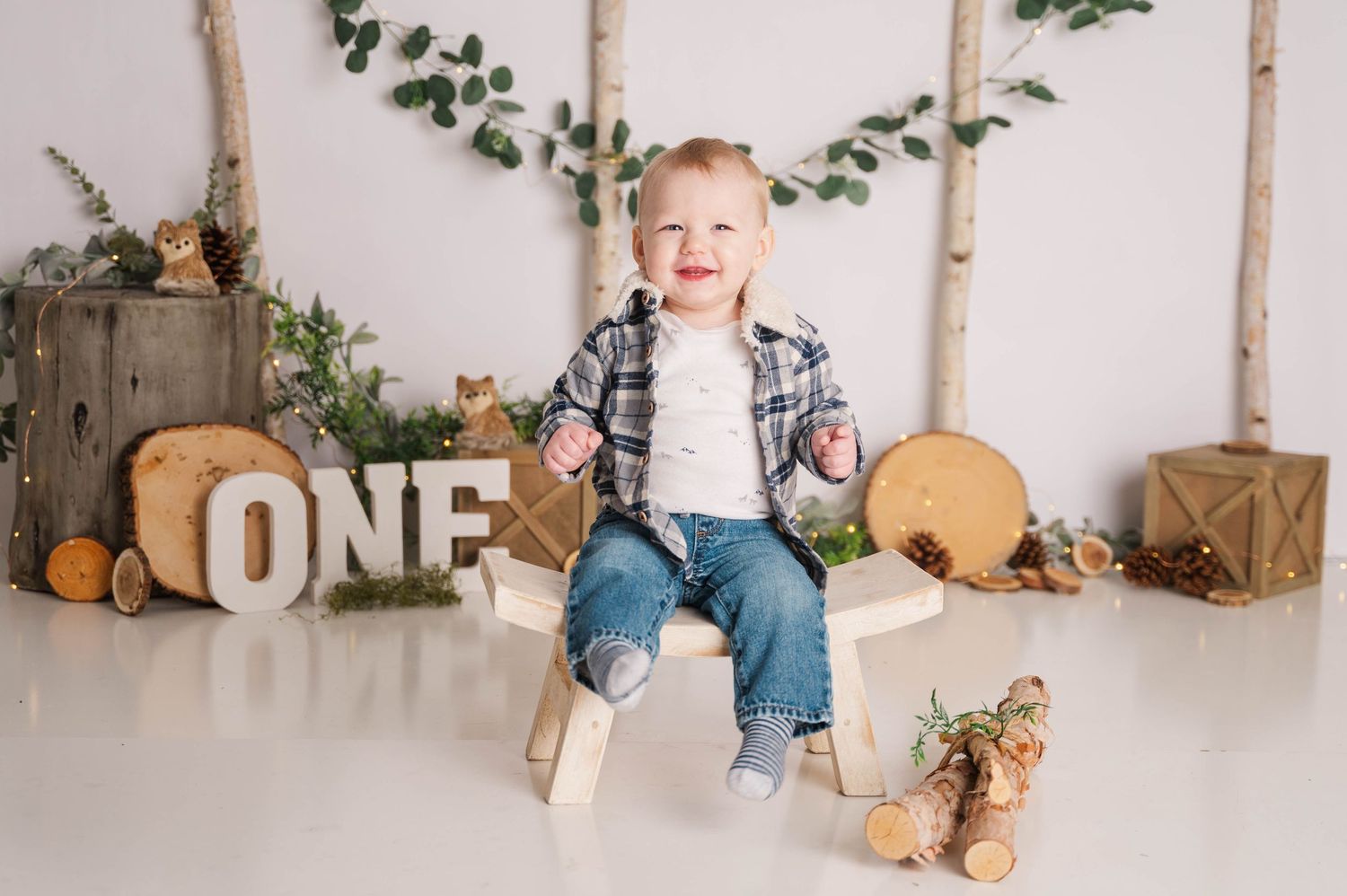 Rustic woodland themed first birthday party setup with birch poles and greenery.