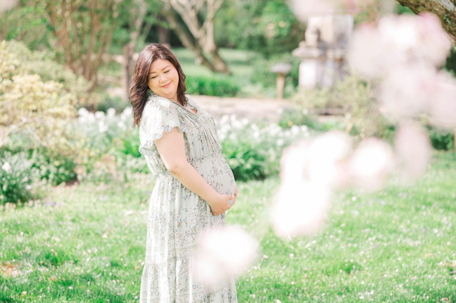 Spring maternity in a garden with blooming flowers and soft bokeh effects.