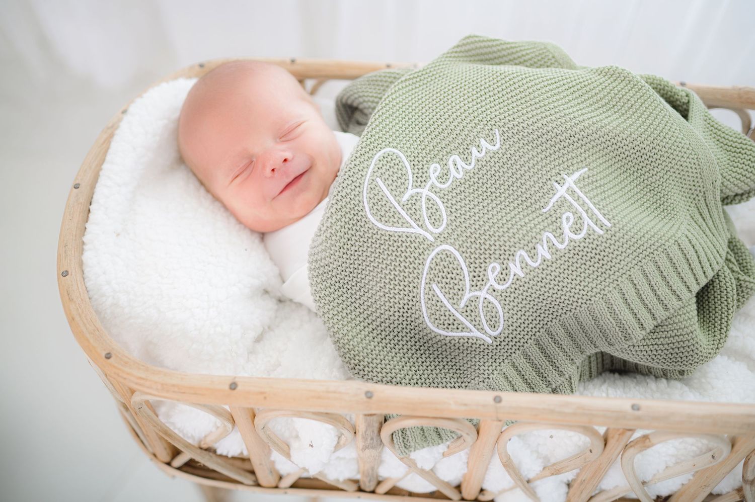 Newborn baby sleeping peacefully under soft sage green knit blanket.