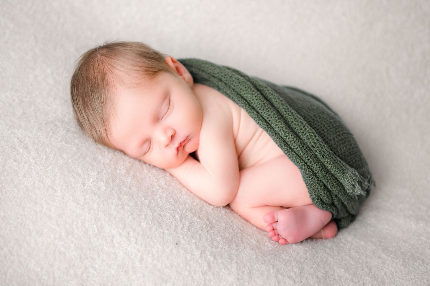 A sleeping newborn baby wrapped in a dark green swaddle
