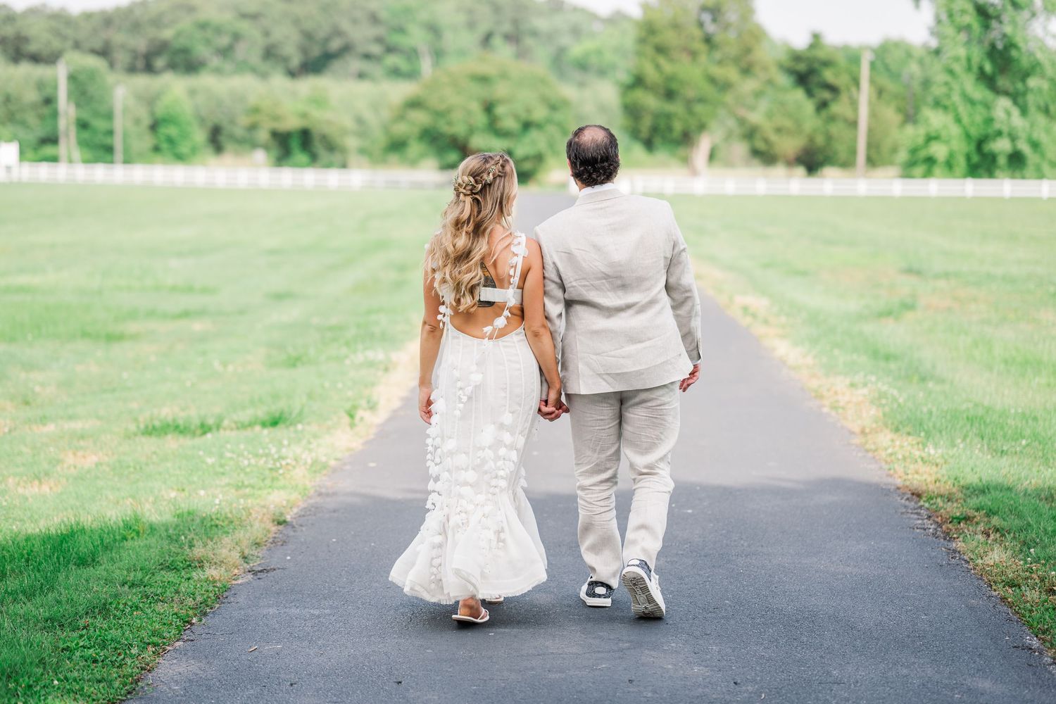 Bride and groom walking hand in hand down a path surrounded by lush green grass on their wedding day.