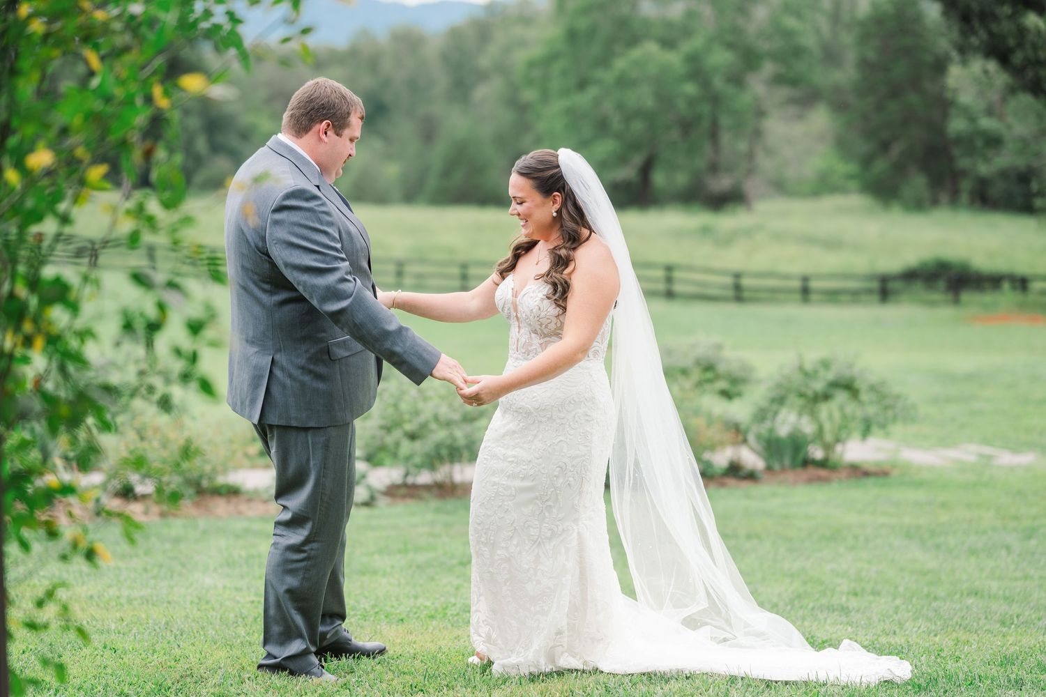 Bride and groom share a tender first look moment on a lush green lawn at an outdoor wedding venue.