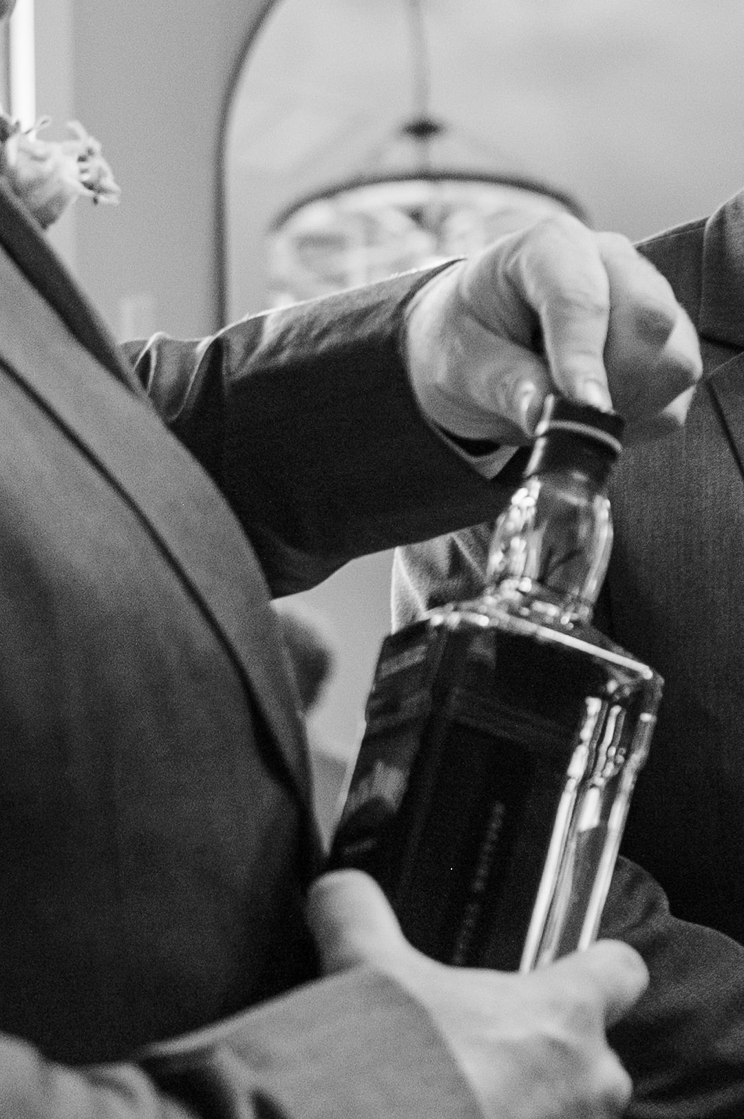 Black and white photo of men in suits pouring whiskey from a bottle at a formal event.