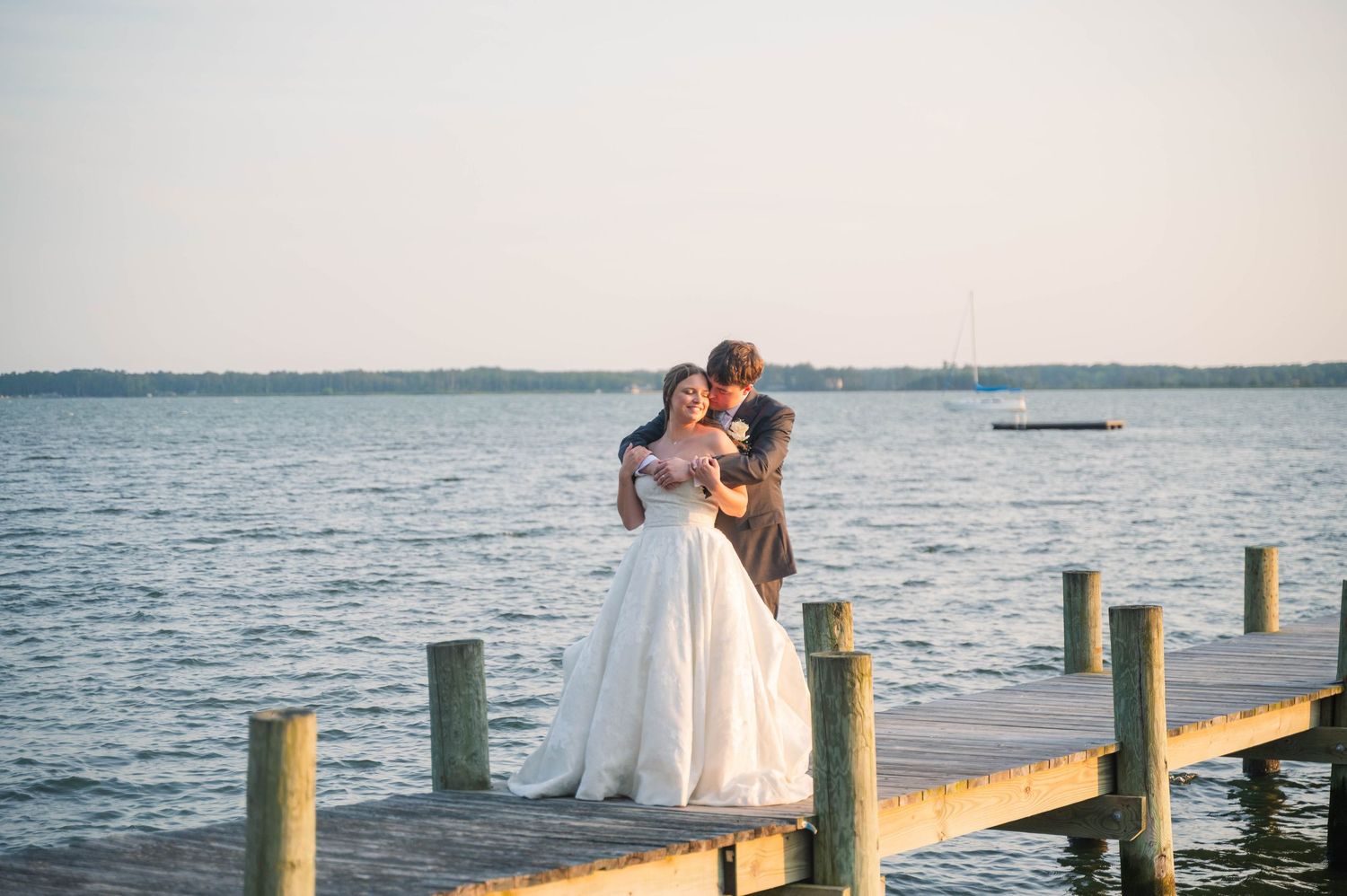 Wedding couple poses on a wooden pier with green posts overlooking a serene waterfront.