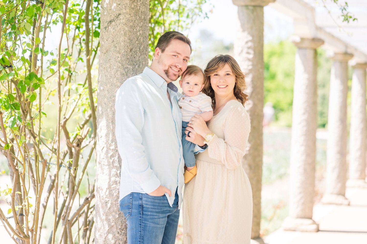 A family sits together on a grassy lawn in casual attire during a sunny outdoor photo session.