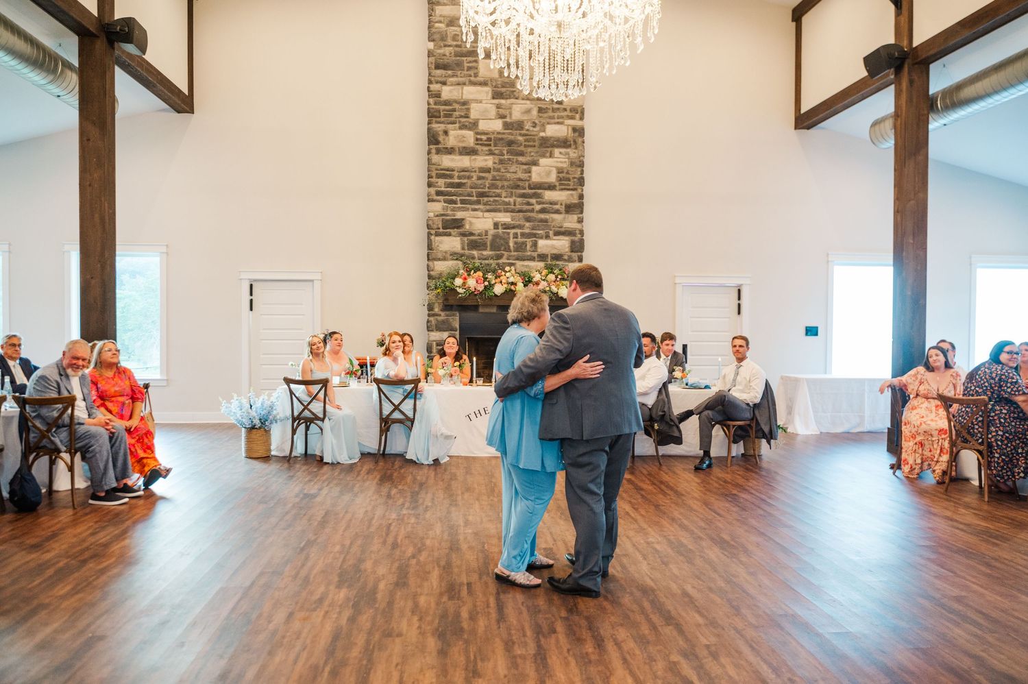Couple shares first dance at elegant wedding reception venue with chandelier and stone fireplace.