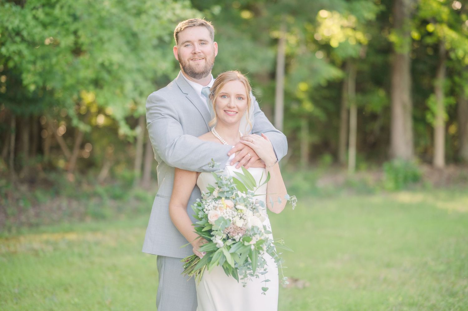 Elegant wedding couple embracing in outdoor garden setting with flowing bouquet.