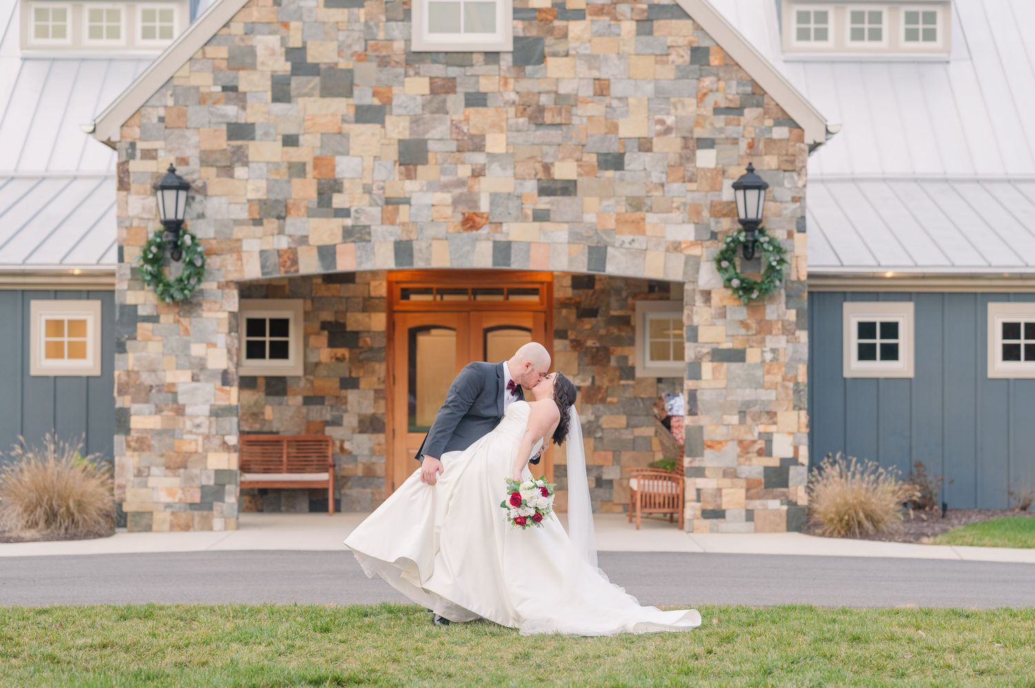 A rustic stone barn with white trim serves as an elegant wedding venue backdrop.