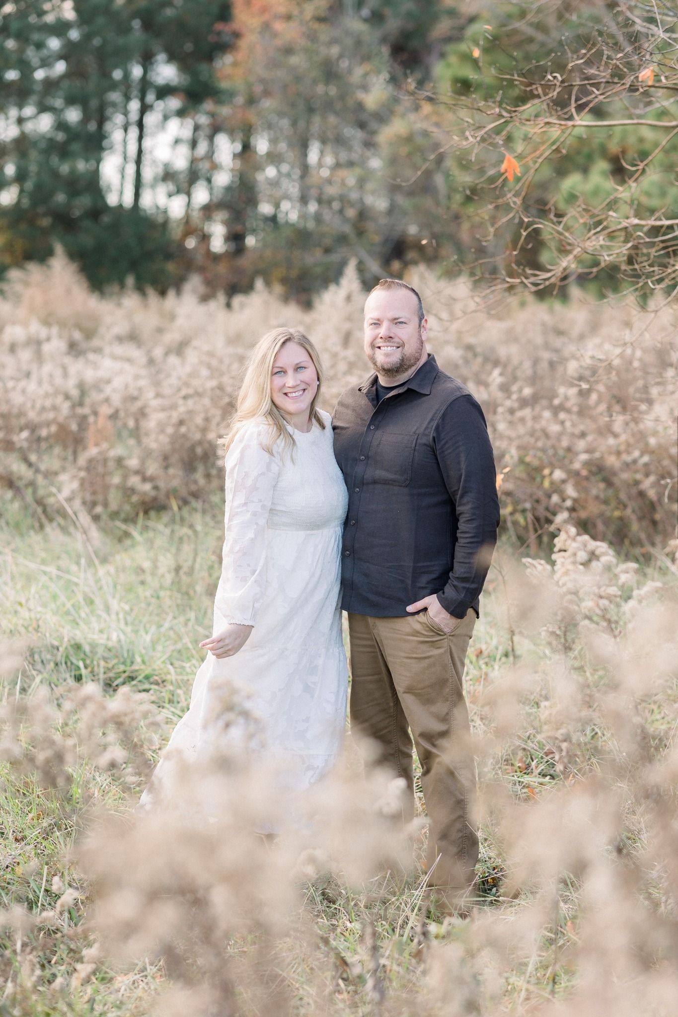 Autumn engagement session in a field with tall grass and fall foliage.