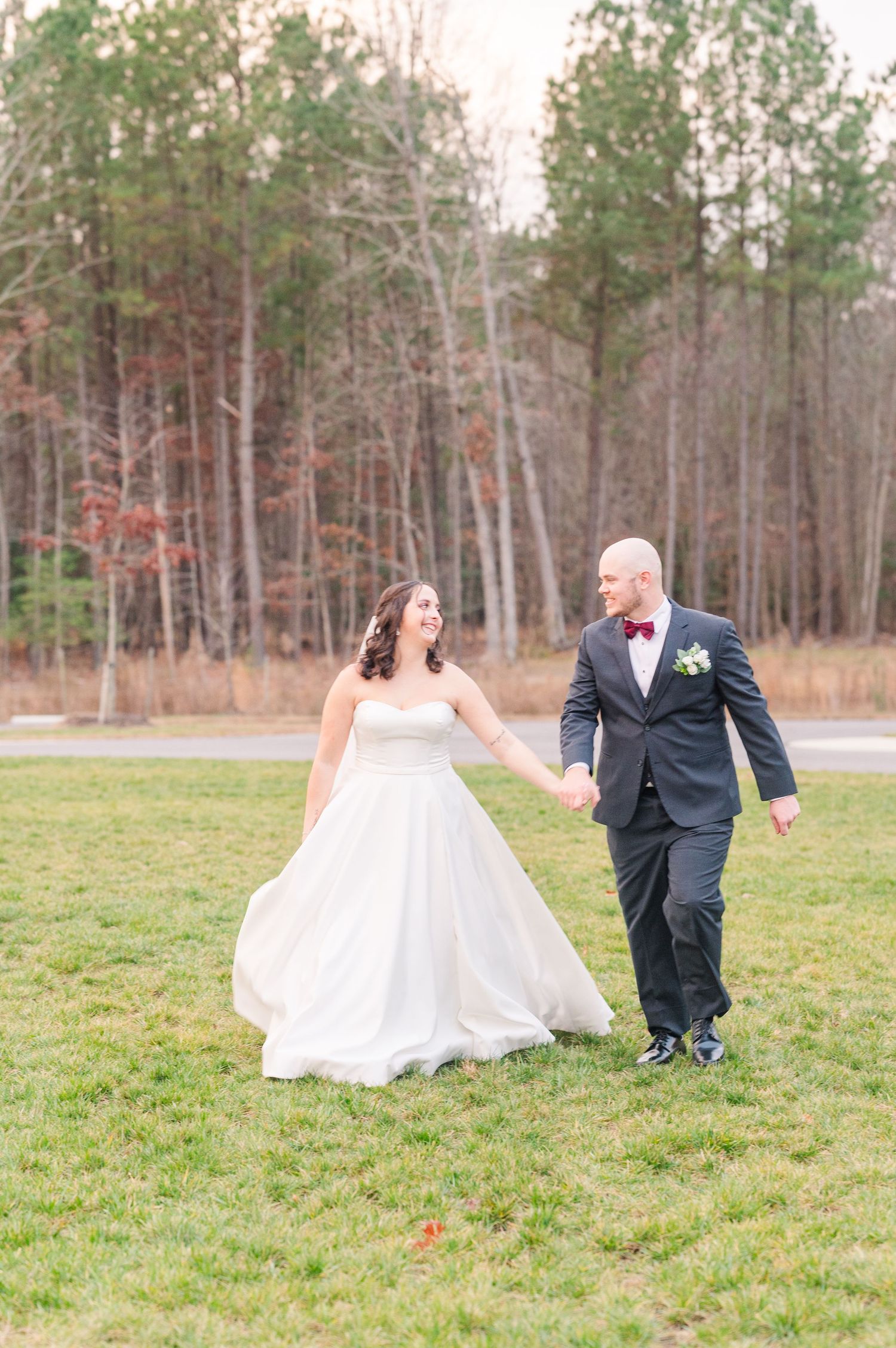 A playful wedding photoshoot in an open field surrounded by winter trees.