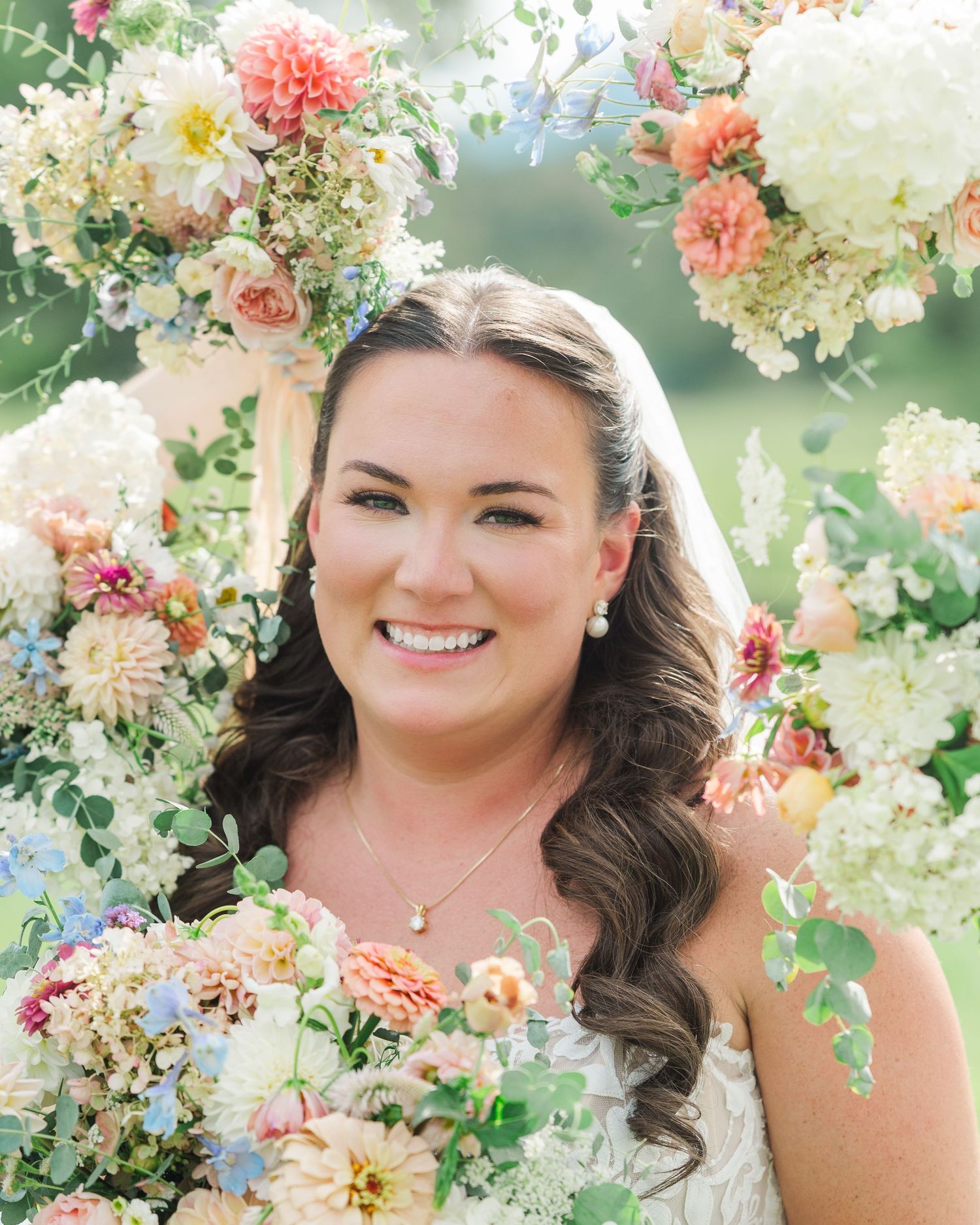 Smiling bride in white gown surrounded by colorful pink and white wedding flowers and greenery.