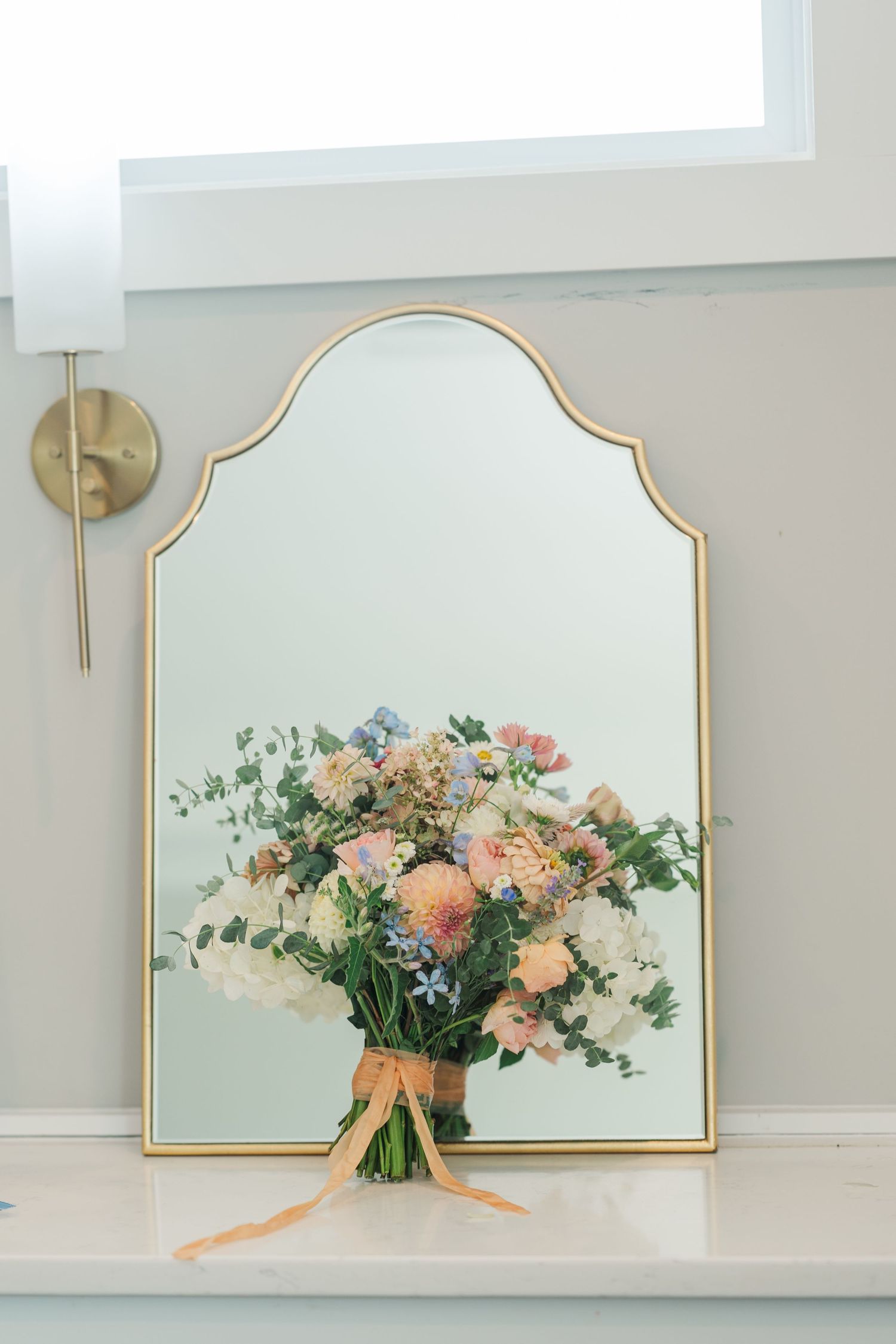 Colorful bridal bouquet with pastel blooms leaning against a gold-framed wall mirror.