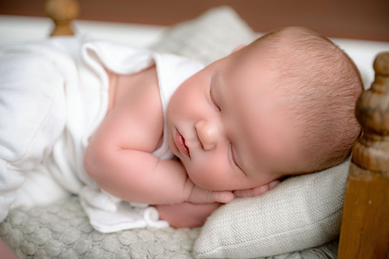 Peaceful sleeping newborn wrapped in white blanket on soft textured surface.