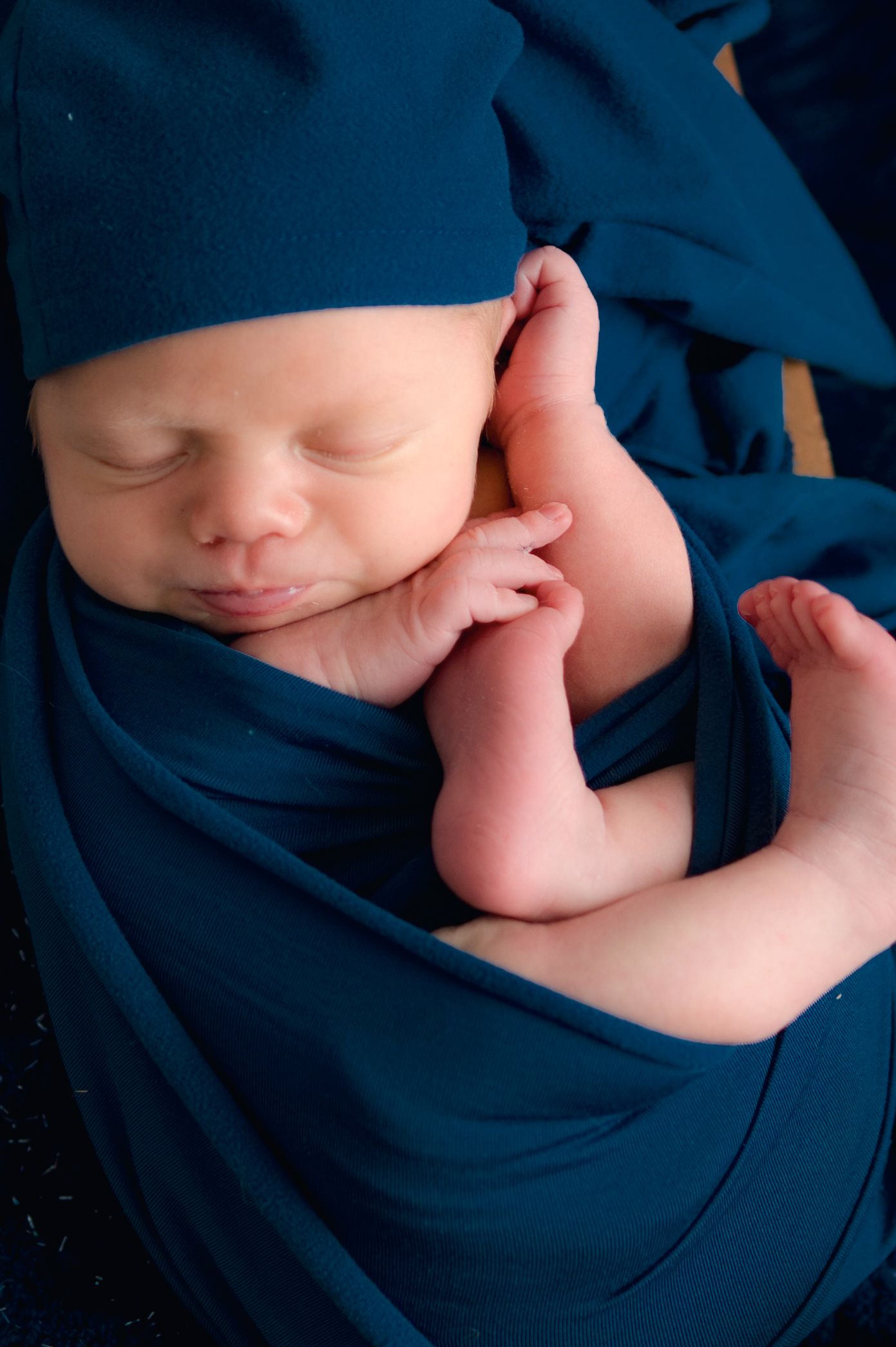 Sleeping newborn wrapped in navy blue blanket in artistic close-up portrait.
