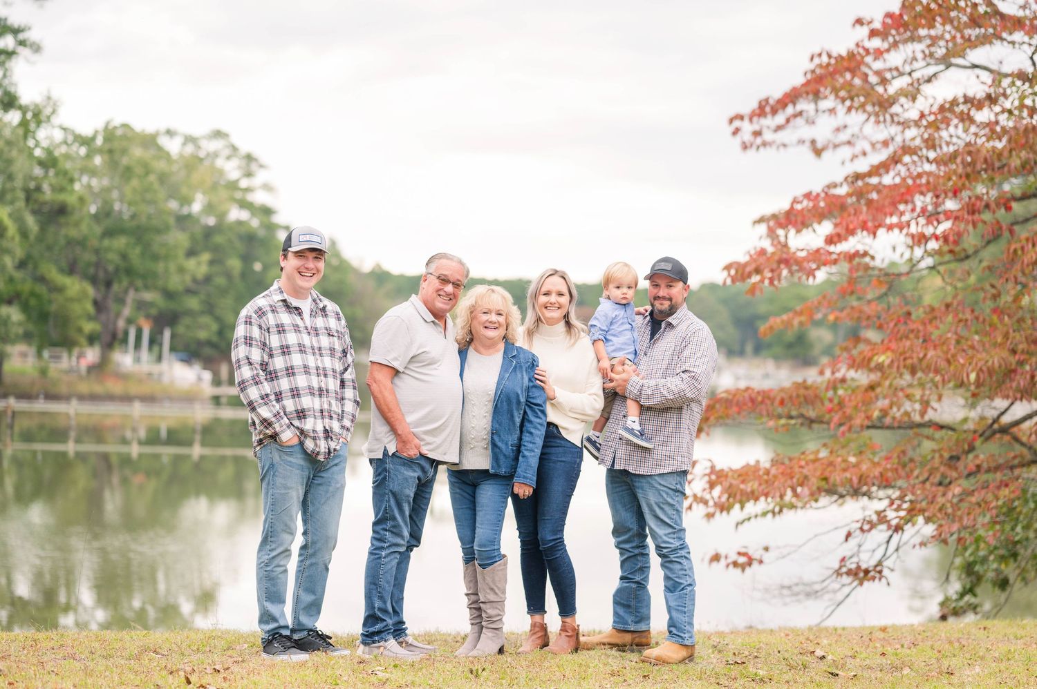 Family group posing together by a lake during golden hour with fall foliage in the background.