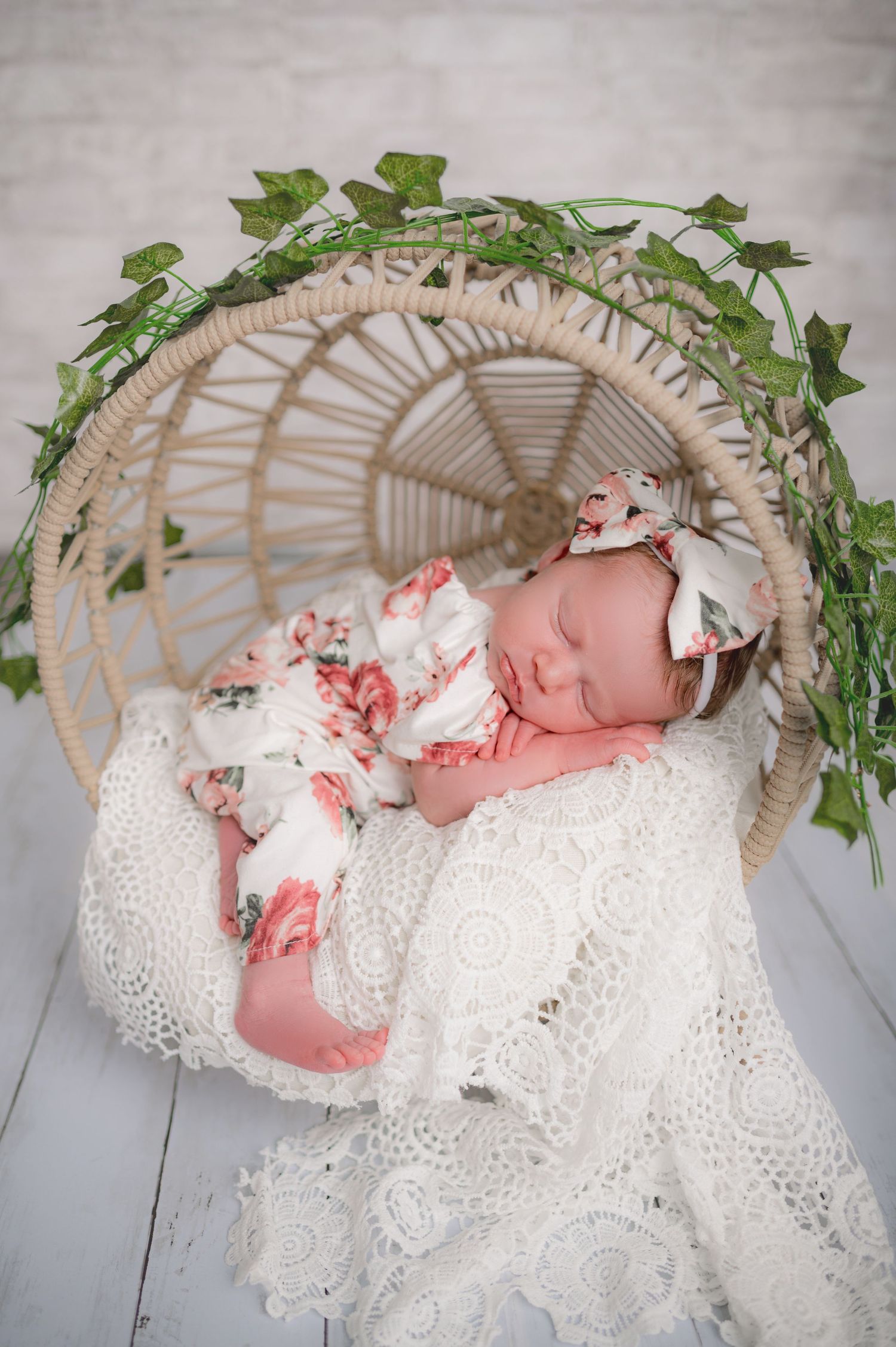 Newborn sleeping peacefully in wicker basket with lace and greenery decorations.