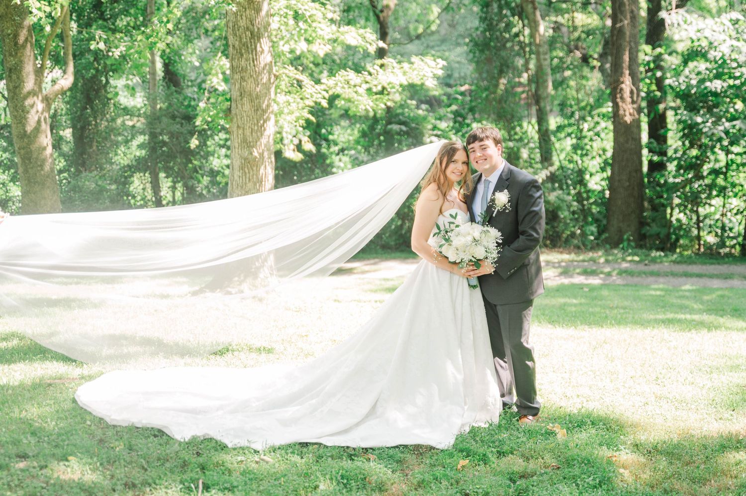 Elegant bridal portraits with flowing veil against green garden backdrop.