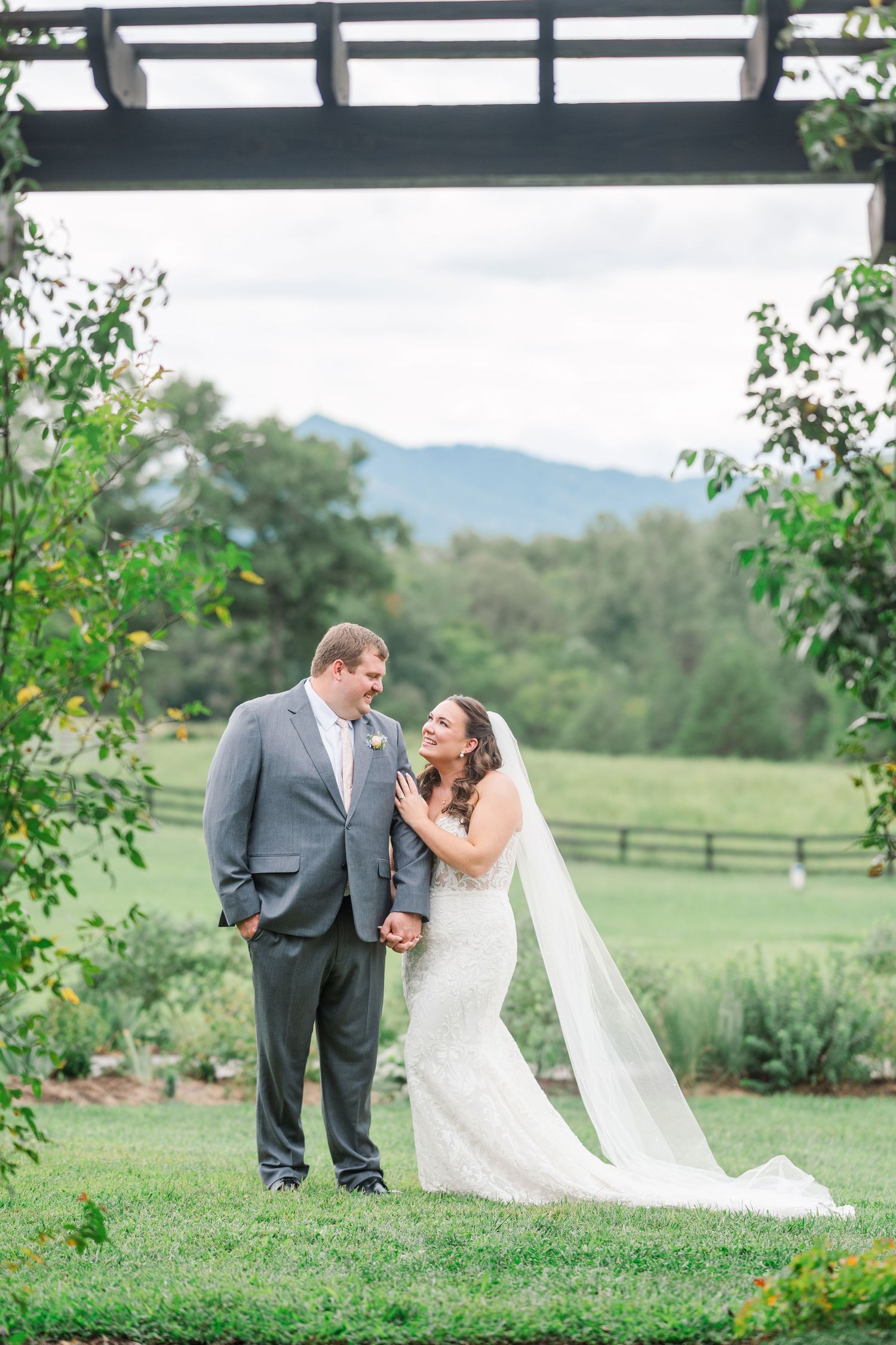 Bride and groom share a tender moment under a wooden pergola with scenic mountain views at an outdoor wedding.