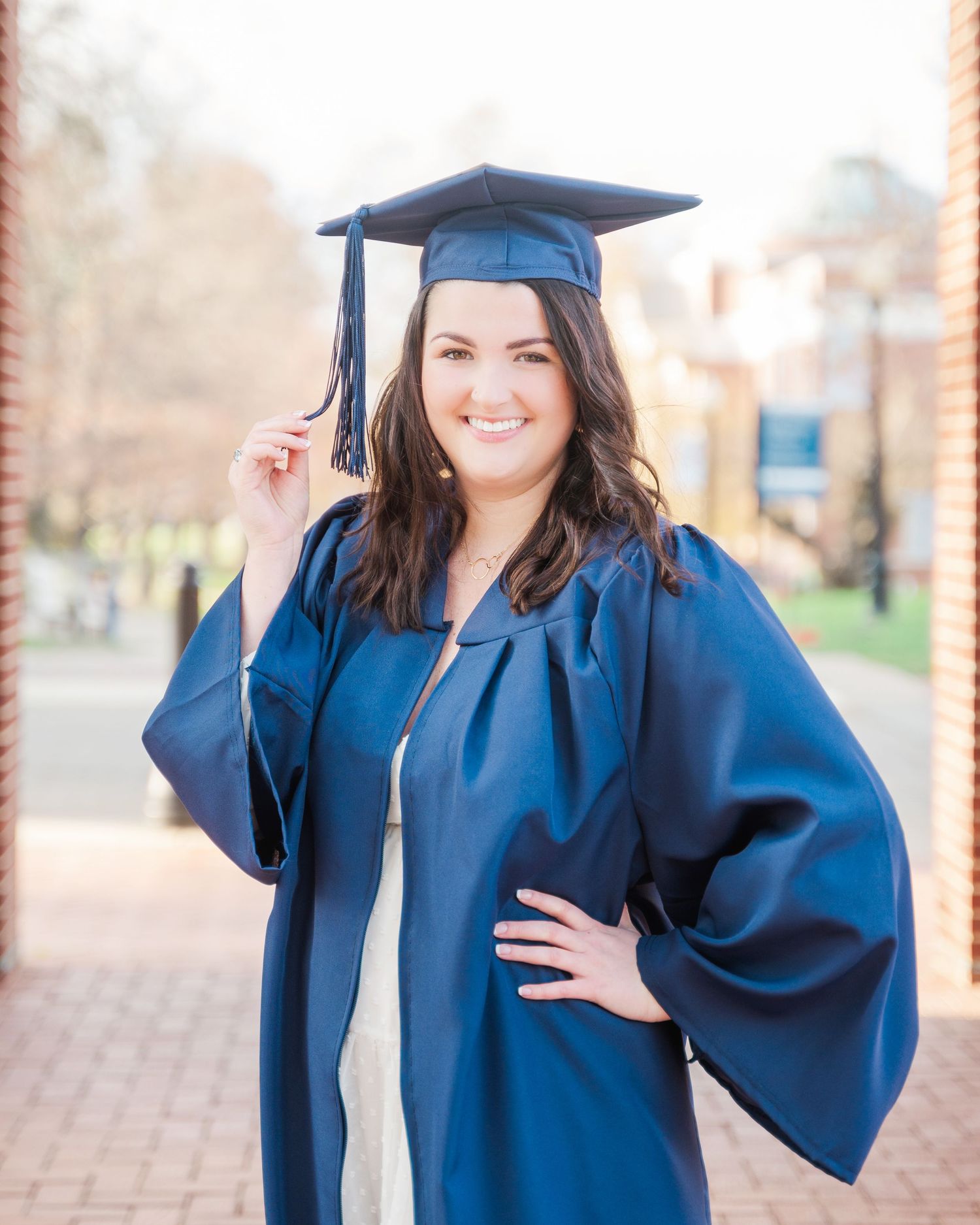 A graduate in navy blue cap and gown poses outdoors during commencement celebrations.