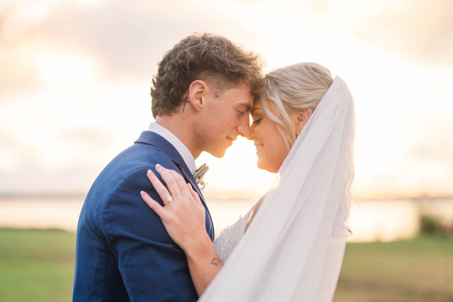 Romantic wedding couple embraces at sunset in a golden field with soft lighting.