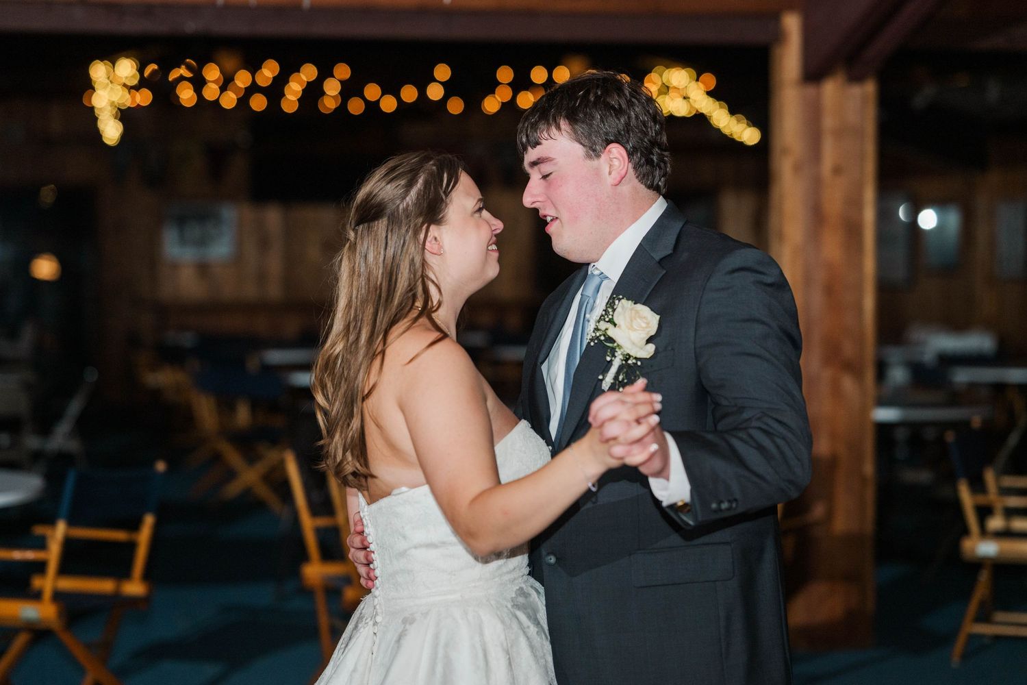 First dance moment at rustic barn wedding venue illuminated by warm string lights.