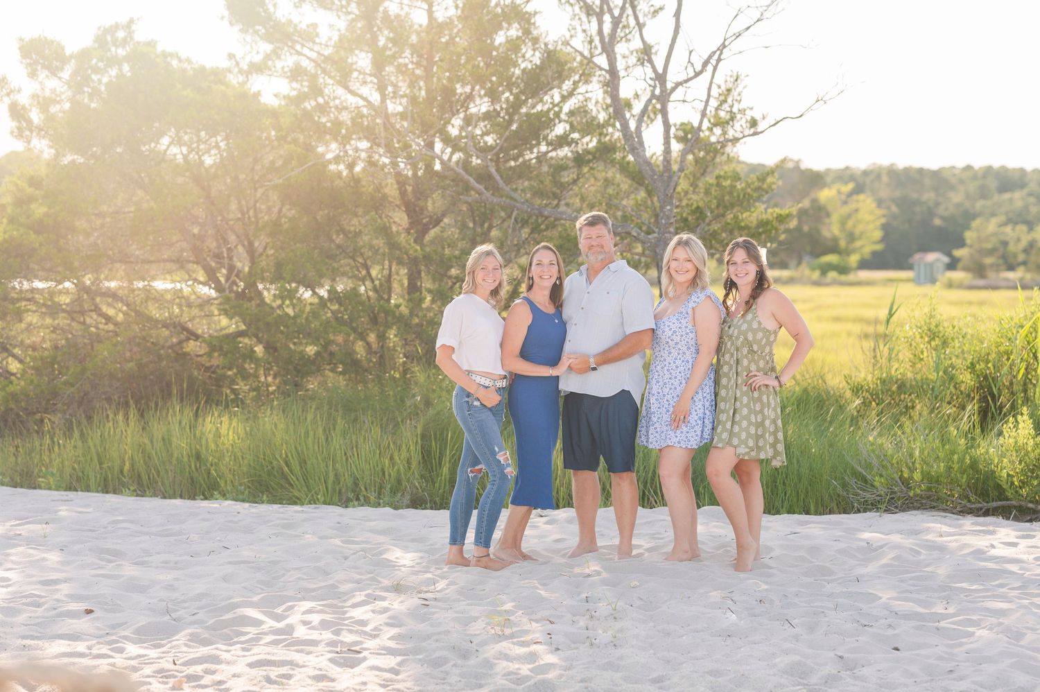 A group poses together on a beach during sunset for a family photo session.