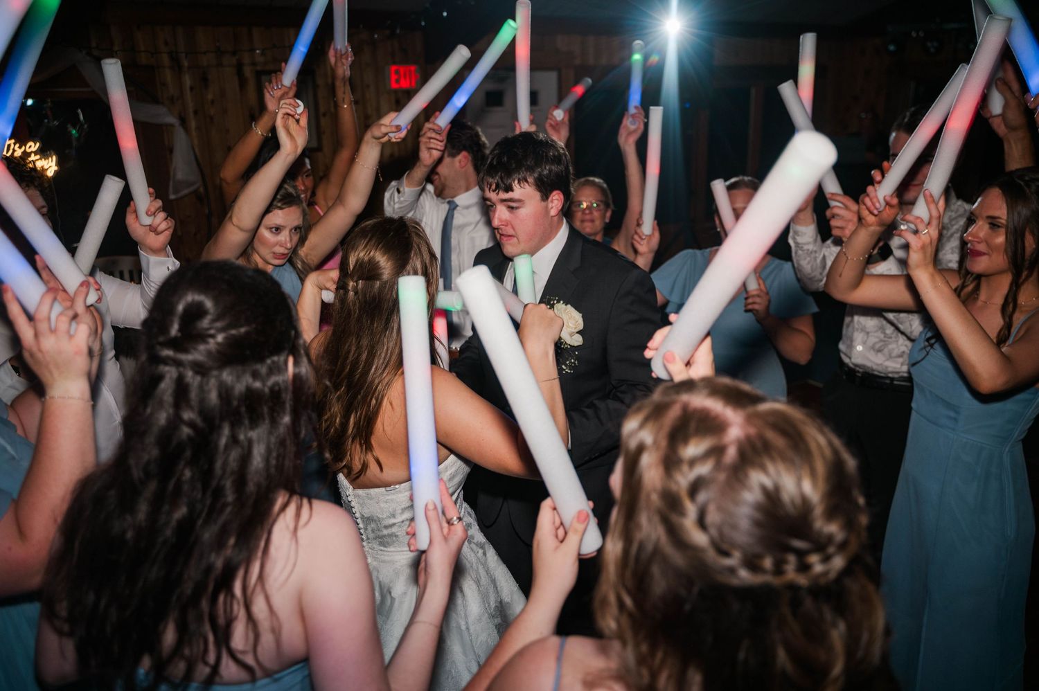 Wedding reception dance party with guests waving colorful LED light sticks on the dance floor.