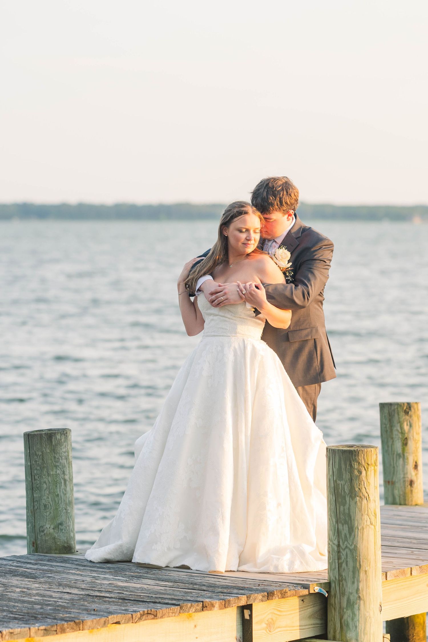 Newlyweds share a romantic moment on a wooden pier with green posts at sunset.
