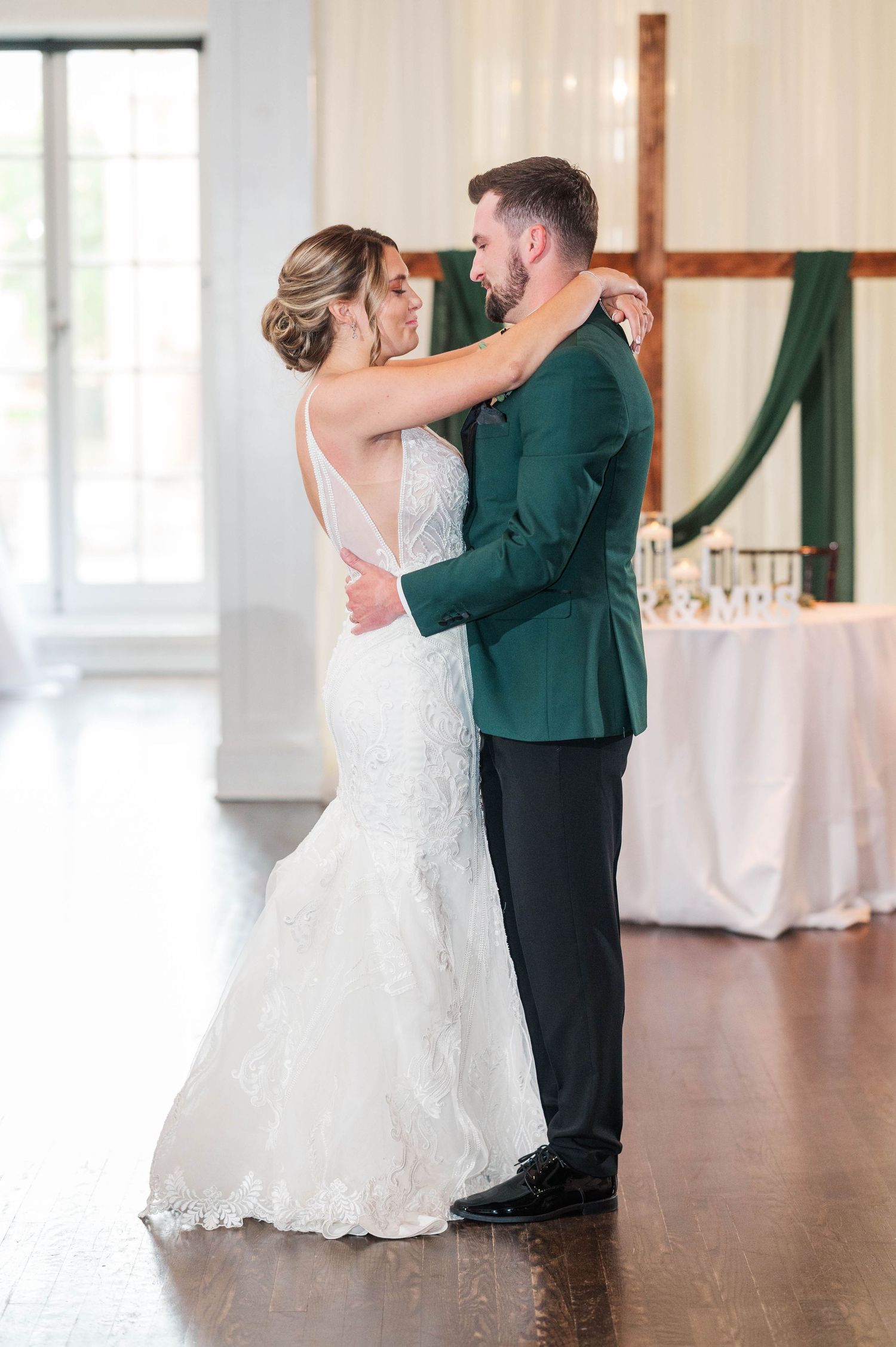 Wedding couple dancing together in sunlit reception venue with white decor.