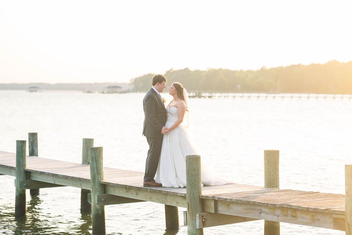 A couple shares a romantic moment on a wooden dock at sunset with water views in the background.
