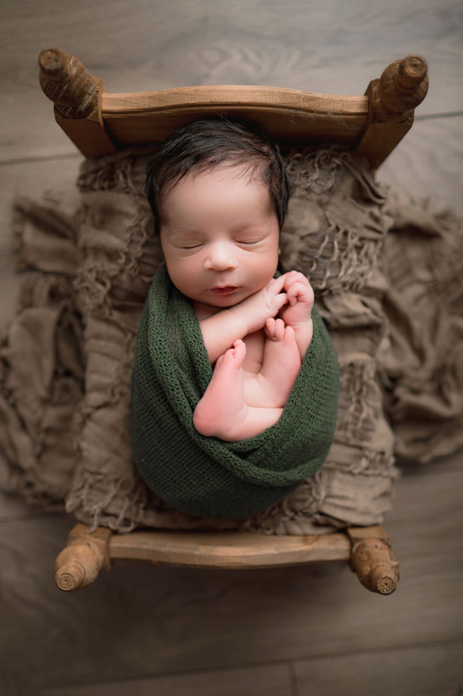 Peaceful newborn swaddled in green wrap lying in vintage wooden bed frame.
