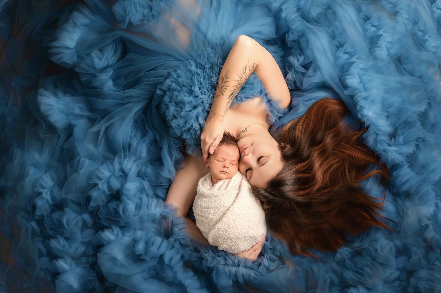 Newborn baby wrapped in white swaddle lying on fluffy blue fabric with flowing hair spread out around them.